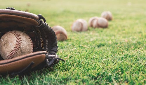 Baseball and Gloves on a grass field with several baseballs on the grass.