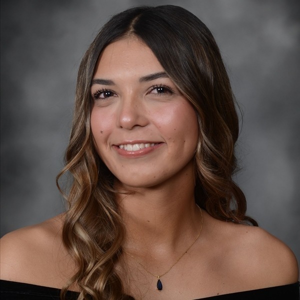 Senior Portrait of Emma Krapcha. She is wearing a black wrap slightly off the shoulders. Her medium brown hair is curled and hanging on her right side. She is wearing a delicate gold chain necklace with a small dark teardroppendant. The portrait is just a headshot, form the chest up.