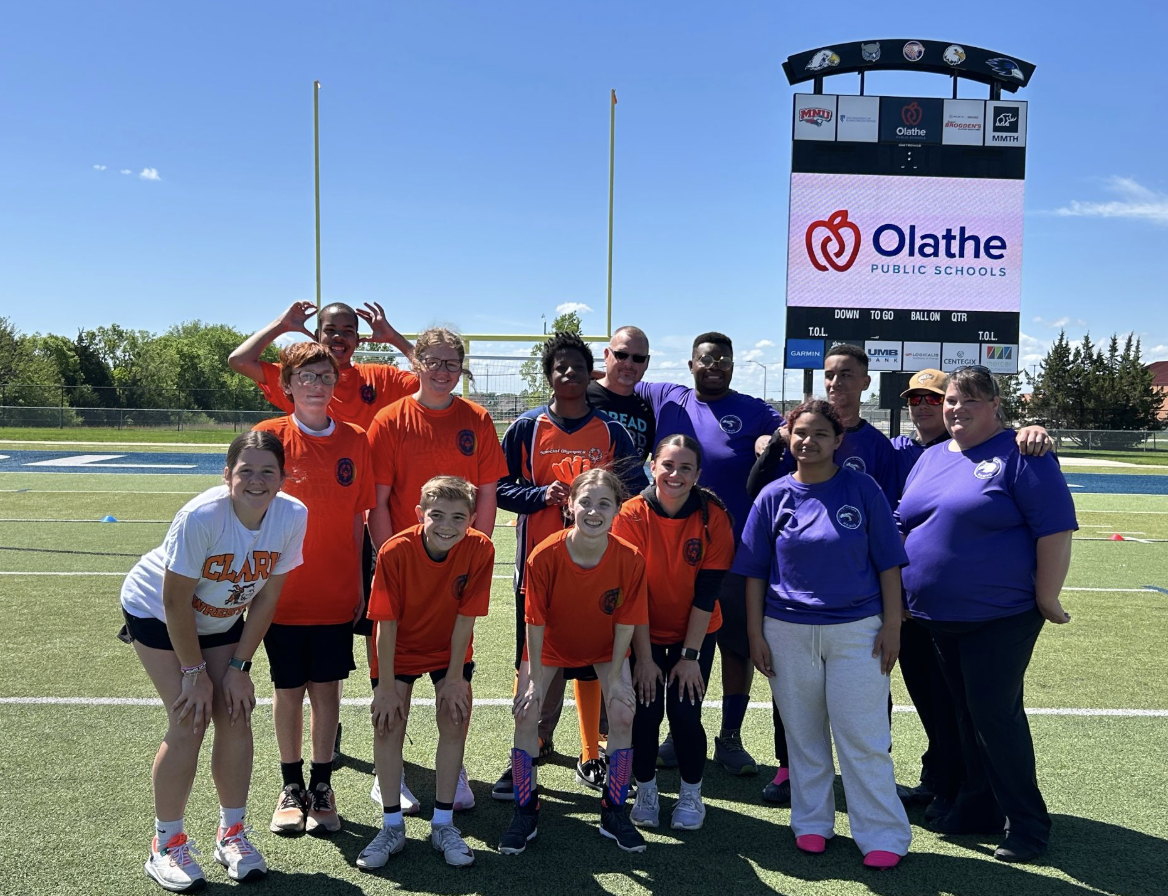 Group of people in orange and white shirts, standing in front of a football field.