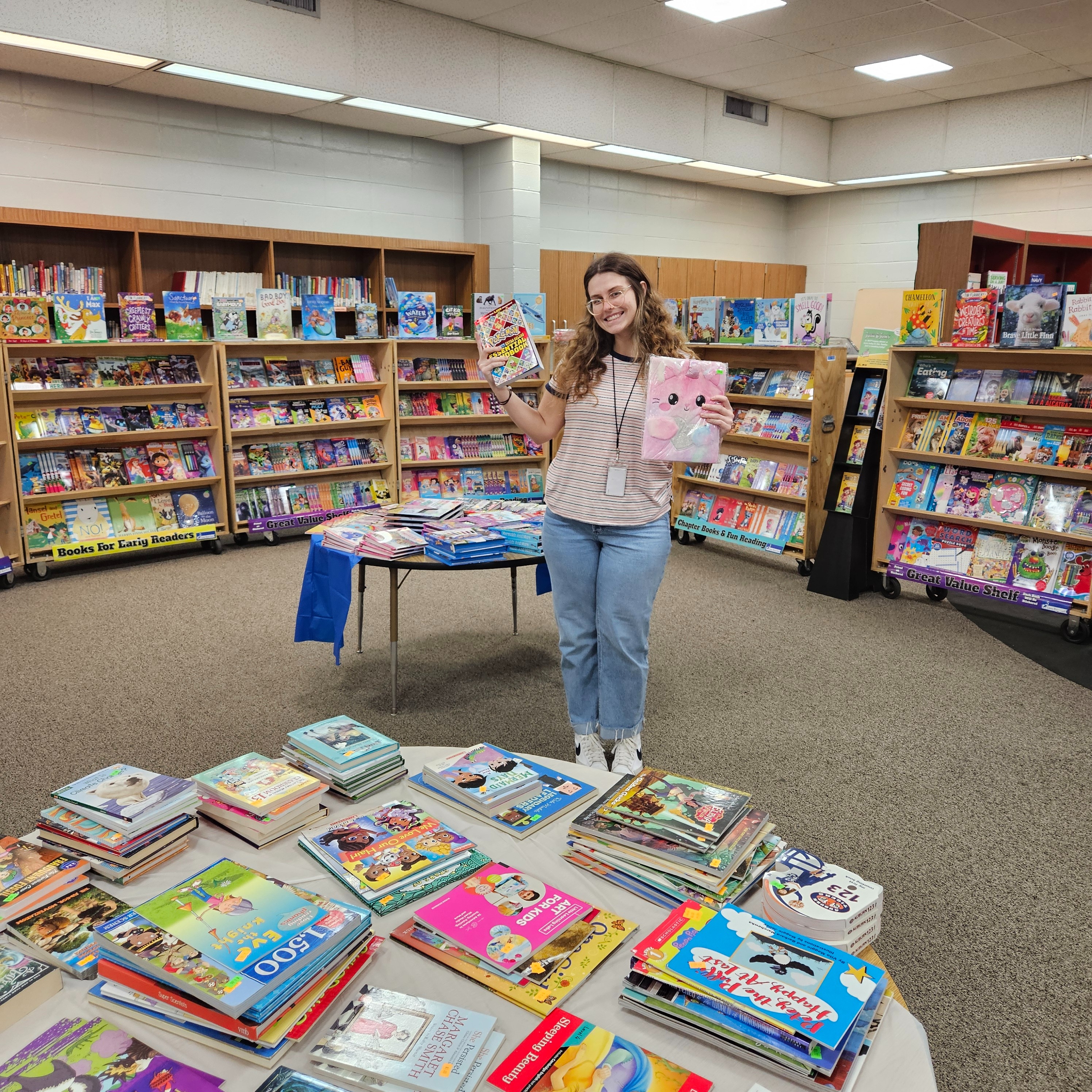 Teacher holding books and the book fair in the library.