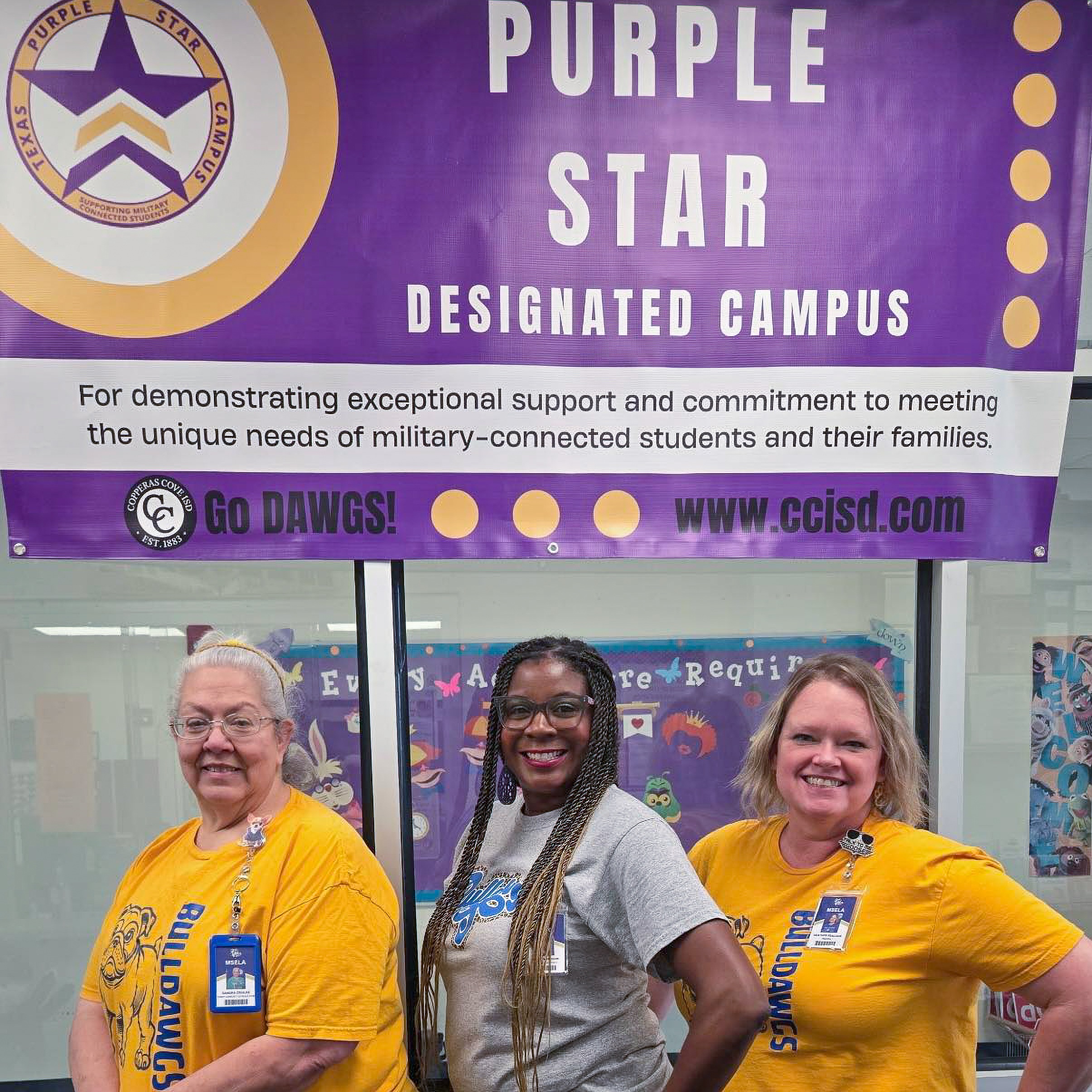 Three women smiling in front of a Purple Star banner