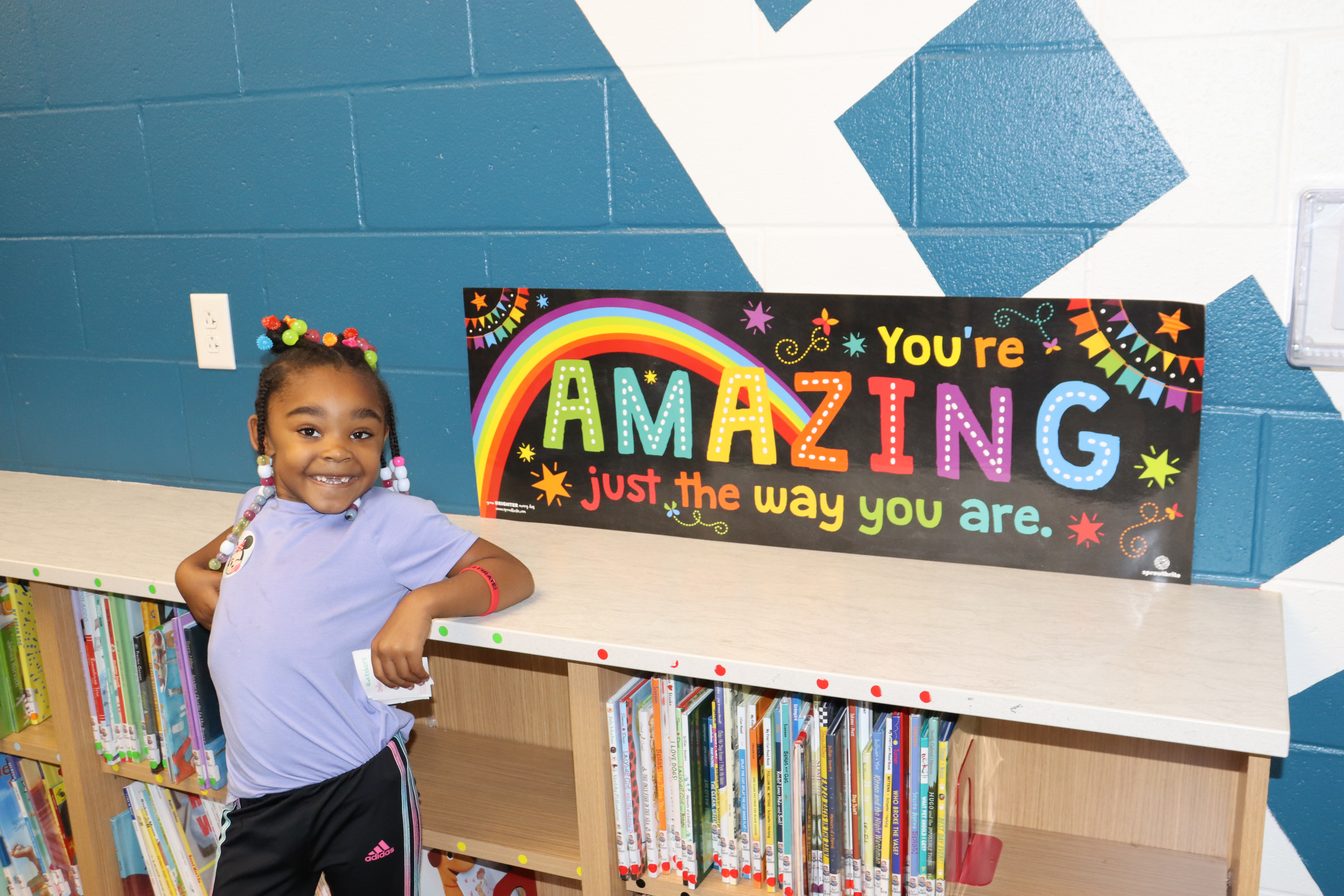 Student standing by sign that says you're amazing just the way you are.