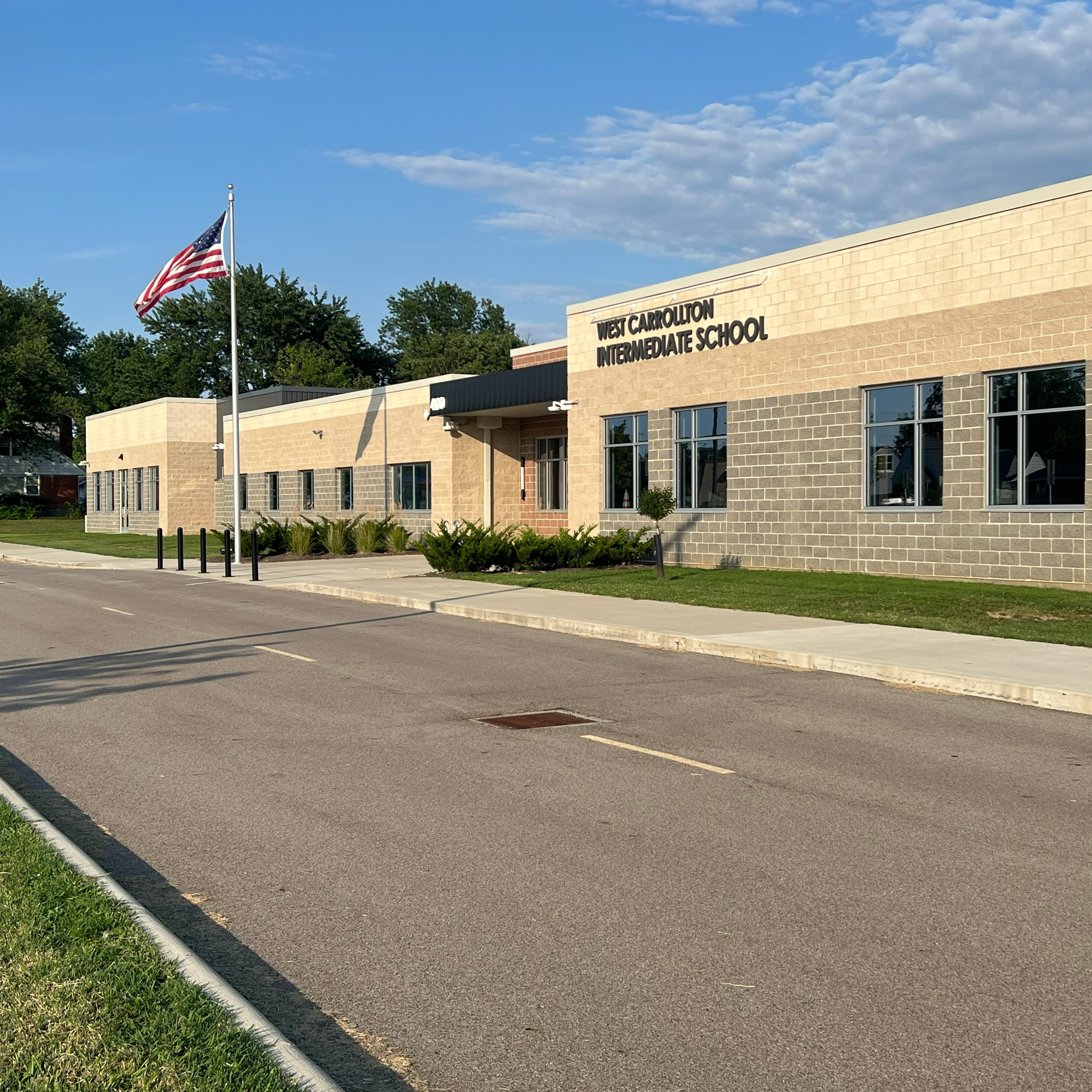 A building with text, an American flag on a pole, and a road leading up to it.