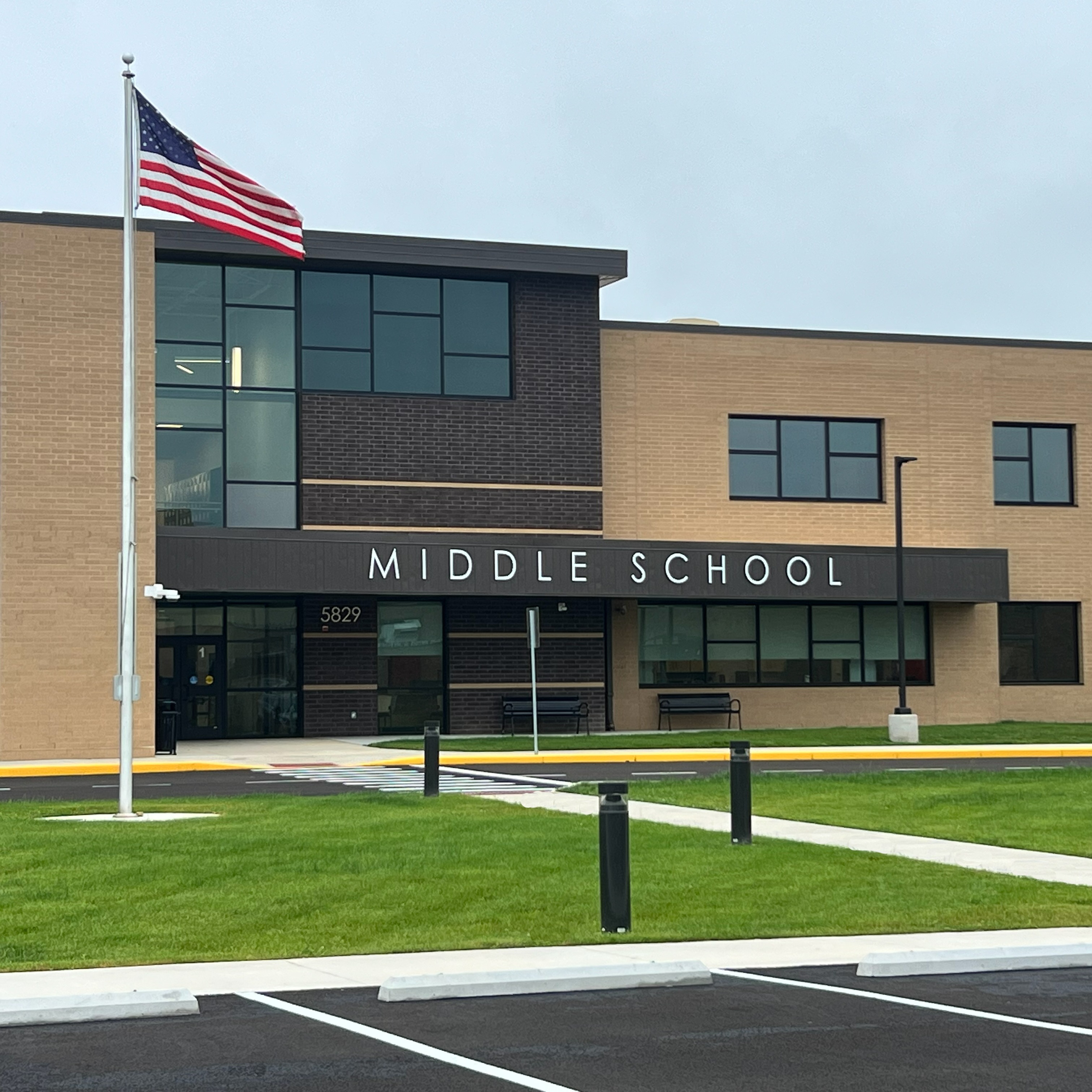 Modern middle school building with flagpole, large windows, and a green lawn in front.
