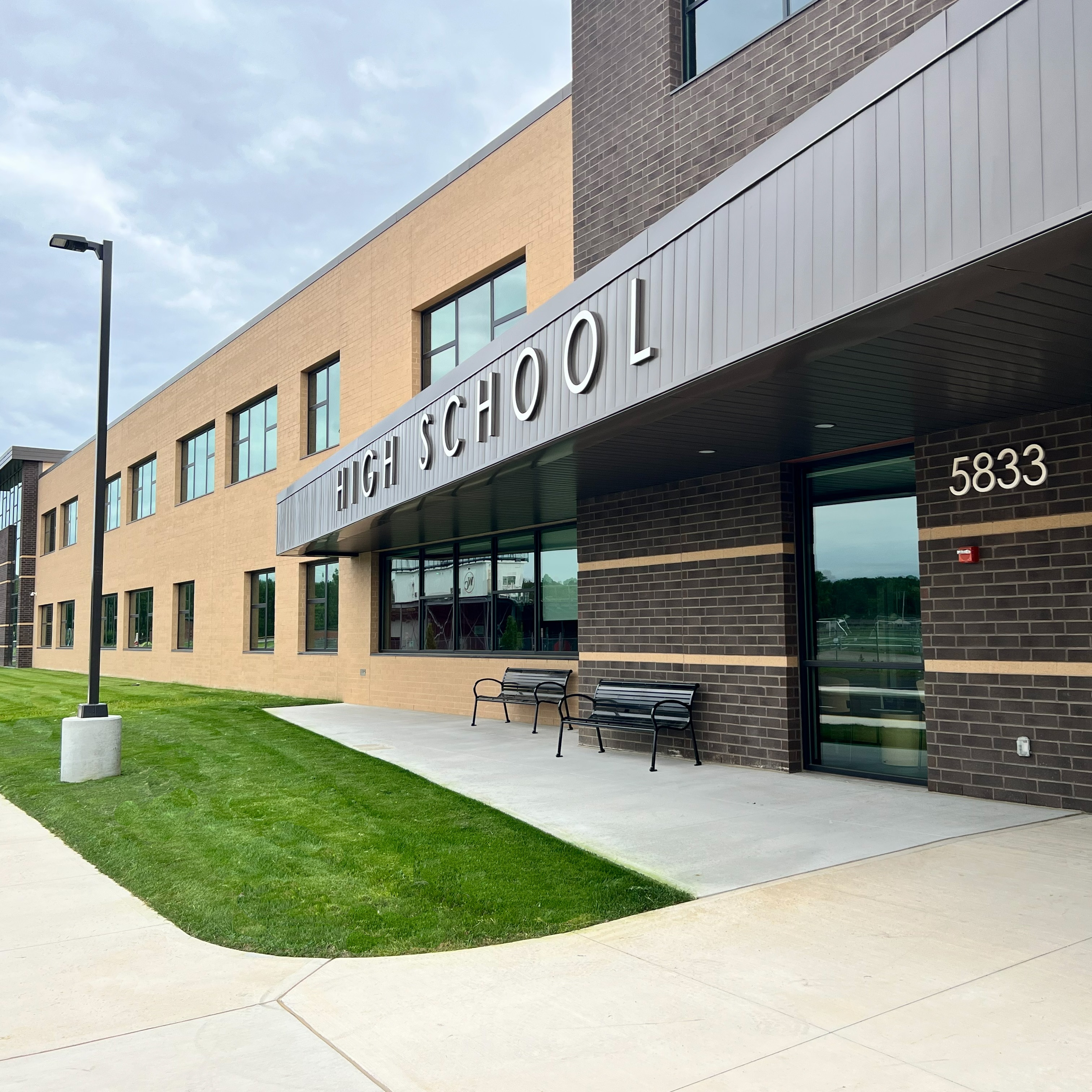 Entrance of a high school building. A large sign reads "HIGH SCHOOL" and number 5833. Two benches sit on the front.