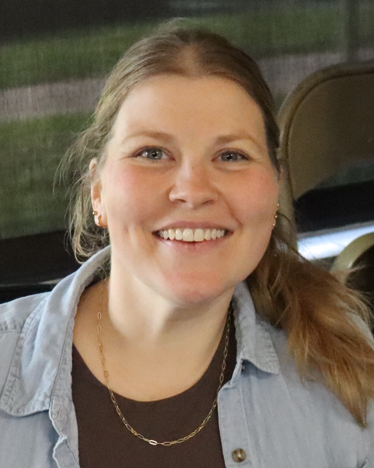 Person with long hair in a brown top and light blue jacket sits at a desk with papers.