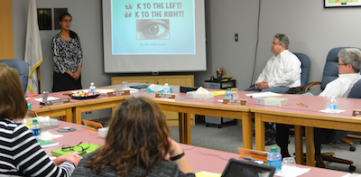 board in a meeting with someone in front leading it and next to her a presentation