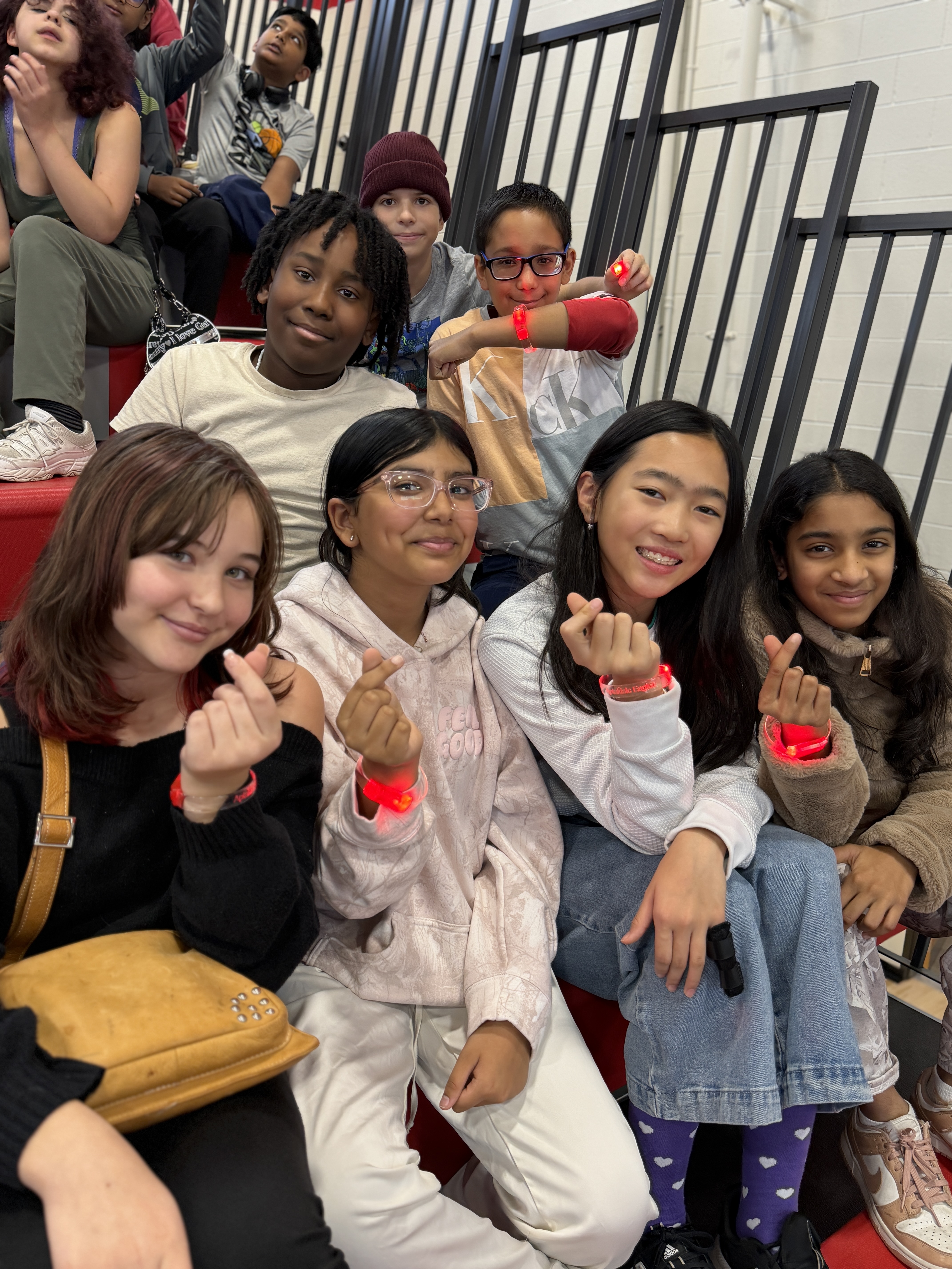 Students sitting in the bleachers holding up their bracelets.
