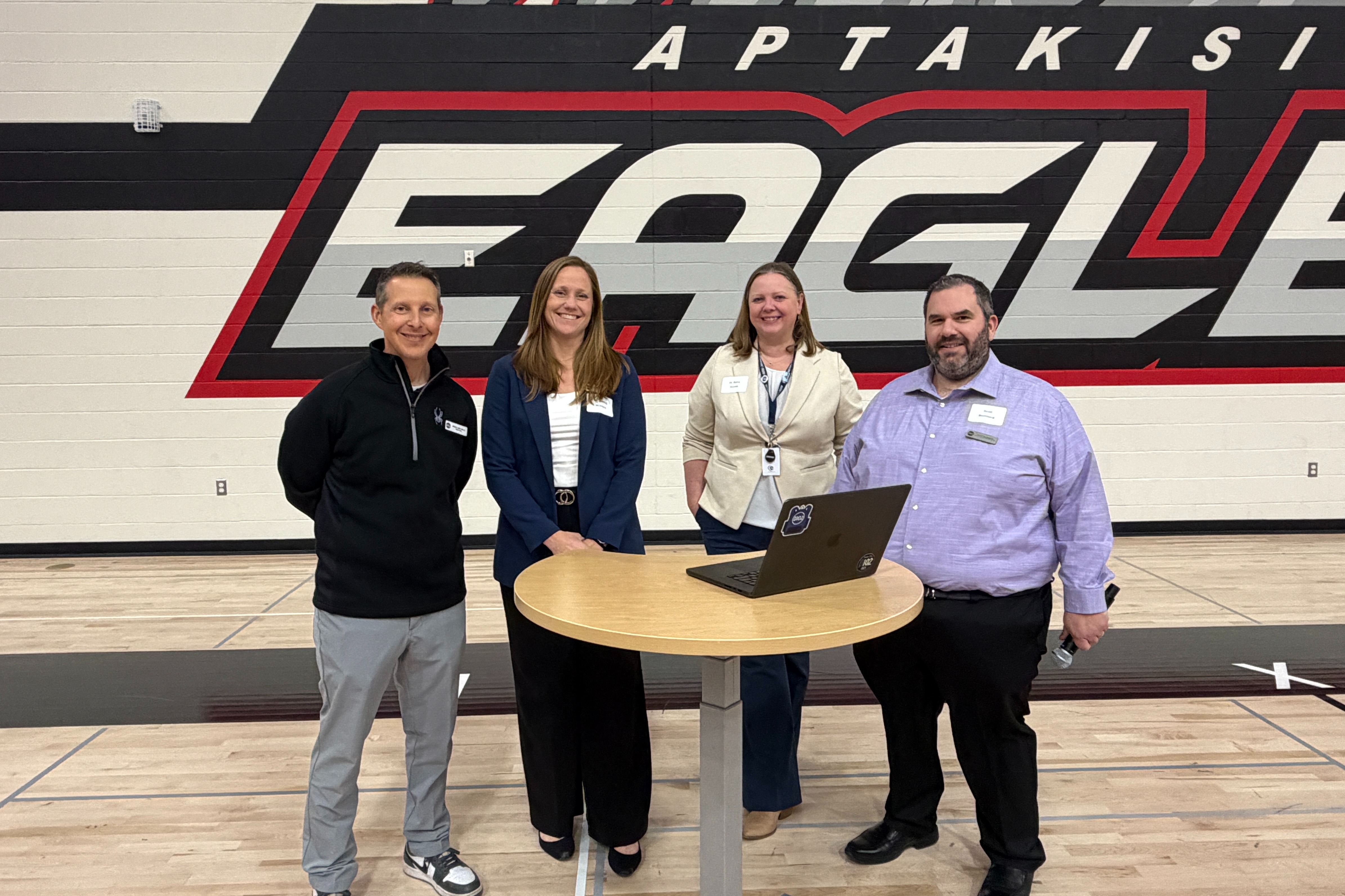 4 staff members standing at a table ready to present in the mega gym.