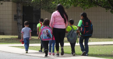 Adult walking with students outside school building