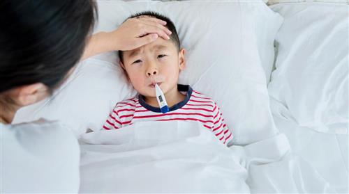boy lying in bed with sad face and thermometer in his mouth