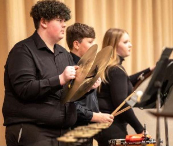 3 students playing the drums in a concert band 