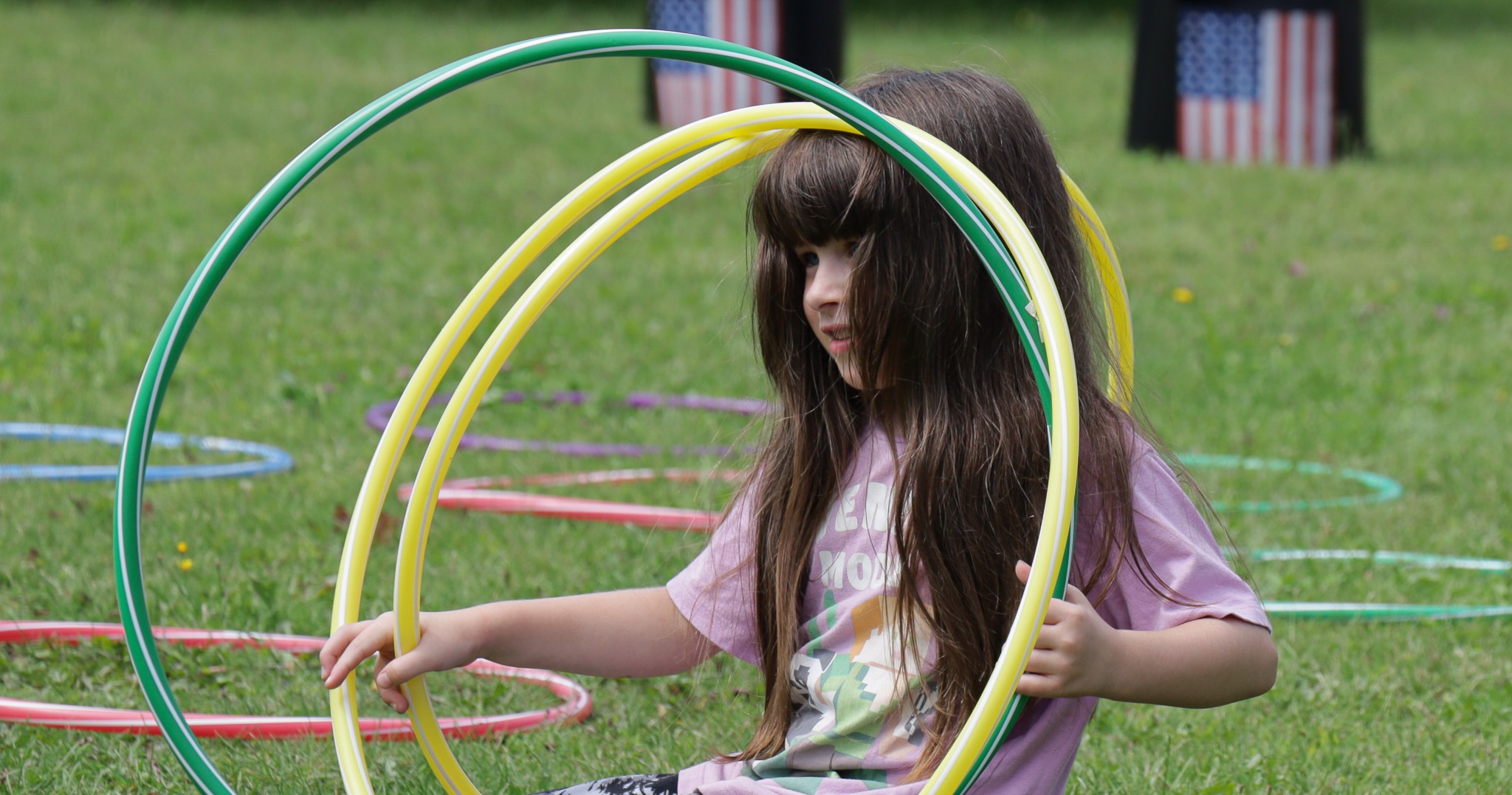 Student sits on grass while playing with colorful hula hoops.