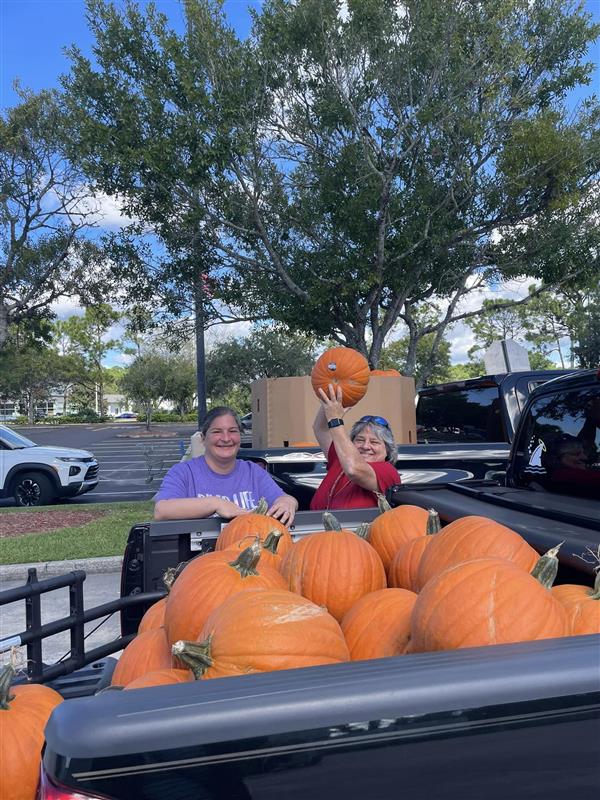 back of a truck full with pumpkins and 2 women’s at the back 