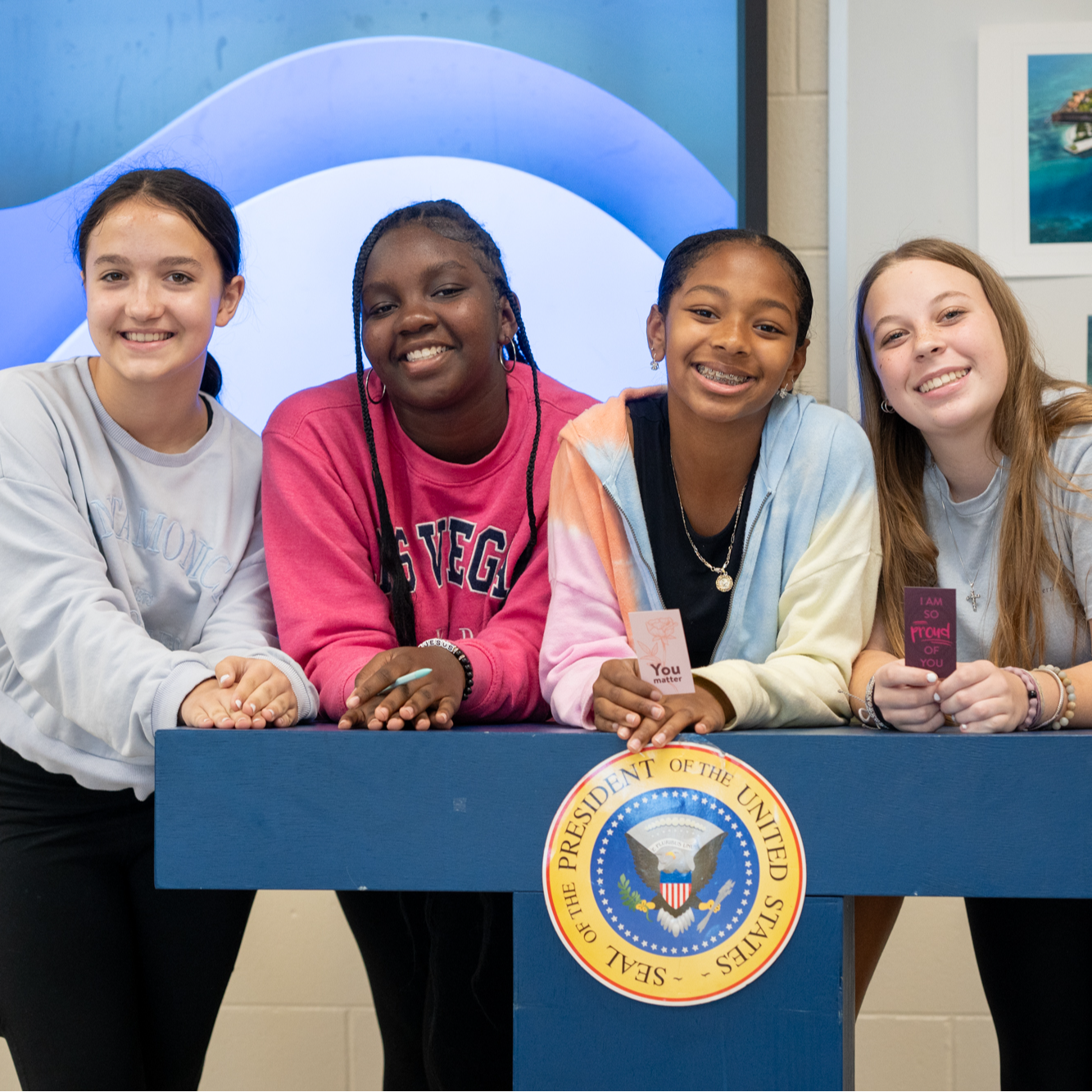 4 Speech and Debate students standing behind a President of The United States Podium
