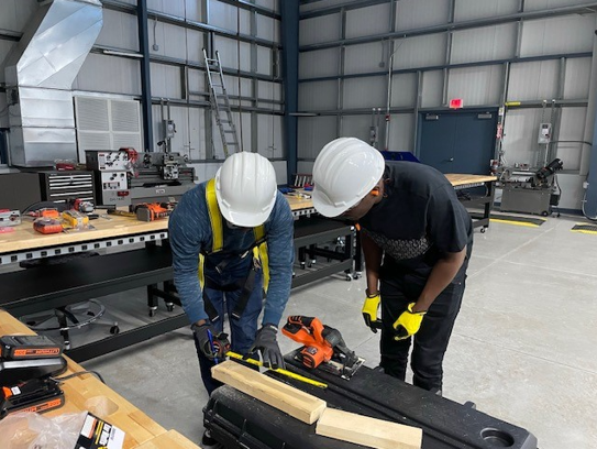 two construction students using a tape measure to measure wood before sawing