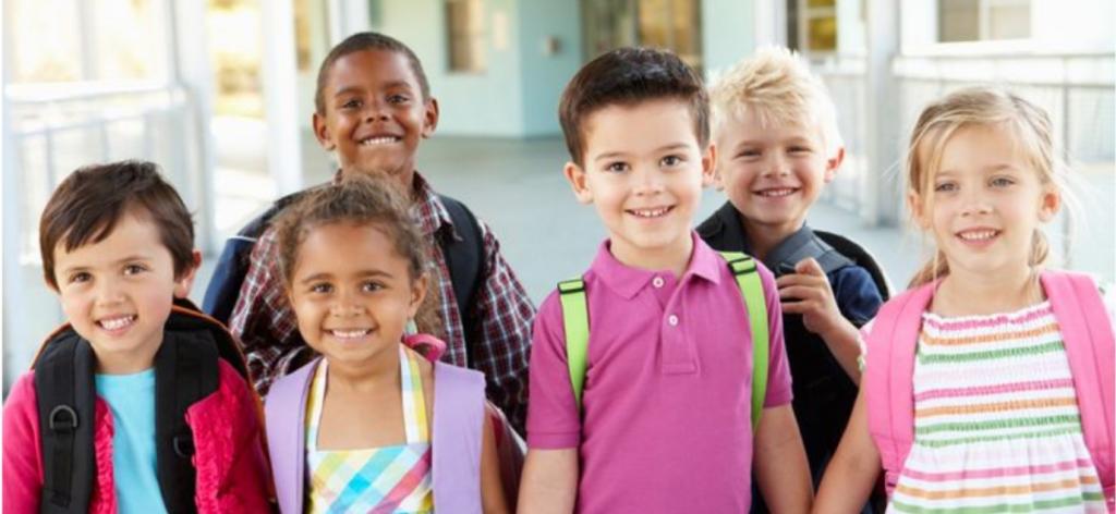 6 kids smiling with backpacks in school