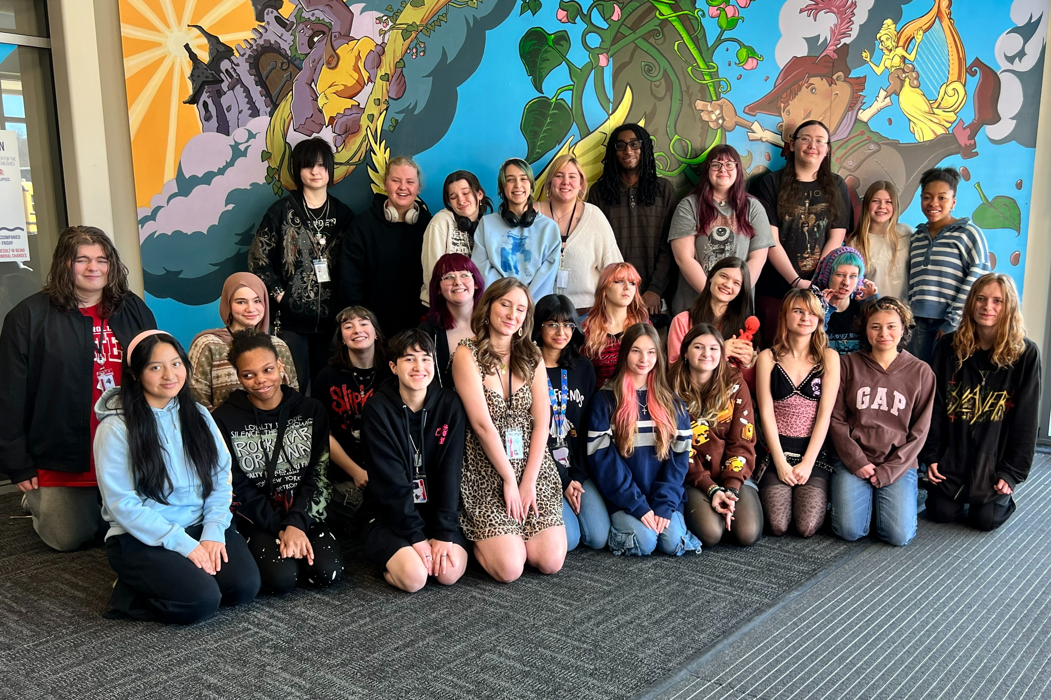 A group of people posing for a photo in a room with a colorful mural on the wall.