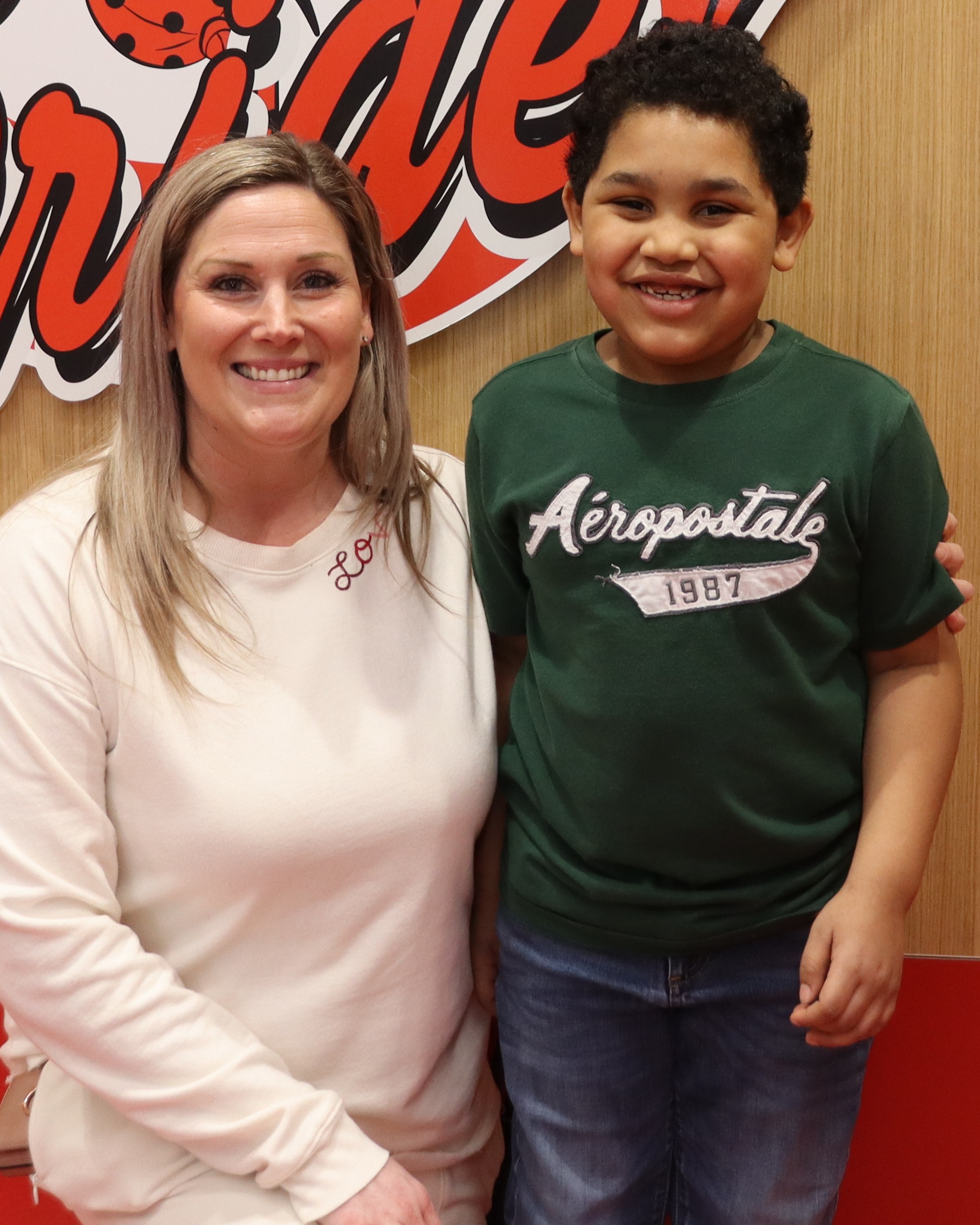Woman and child stand before a sign with pirate logo, wooden and red wall.