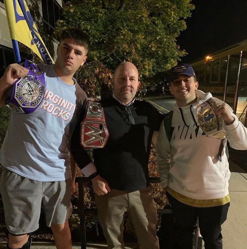 Three boys each of them holding a wrestling belt while posing for a picture.