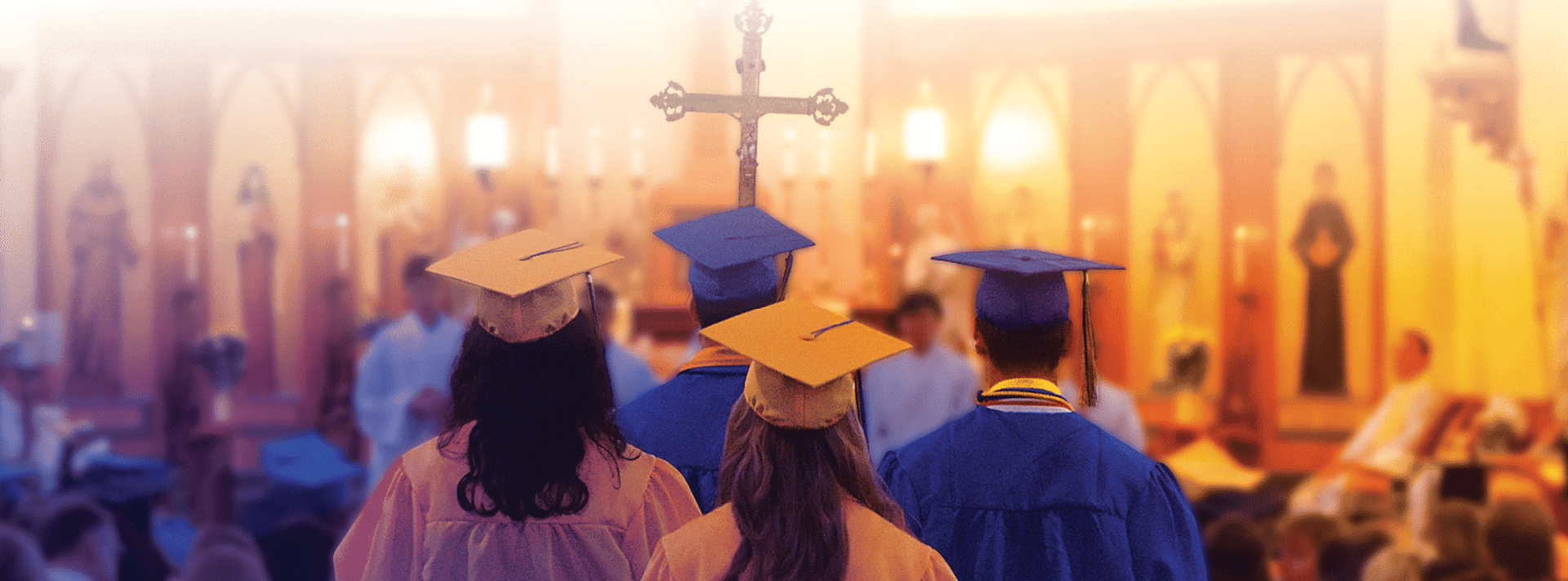 students in graduation gowns walking with a cross 