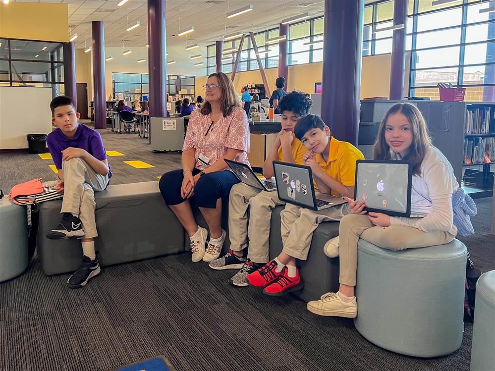 students sitting using their laptops with a teacher beside them