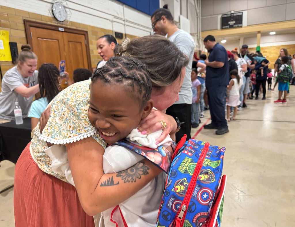 A student and teacher are smiling and hugging one another during the school's Back to School Night event. 