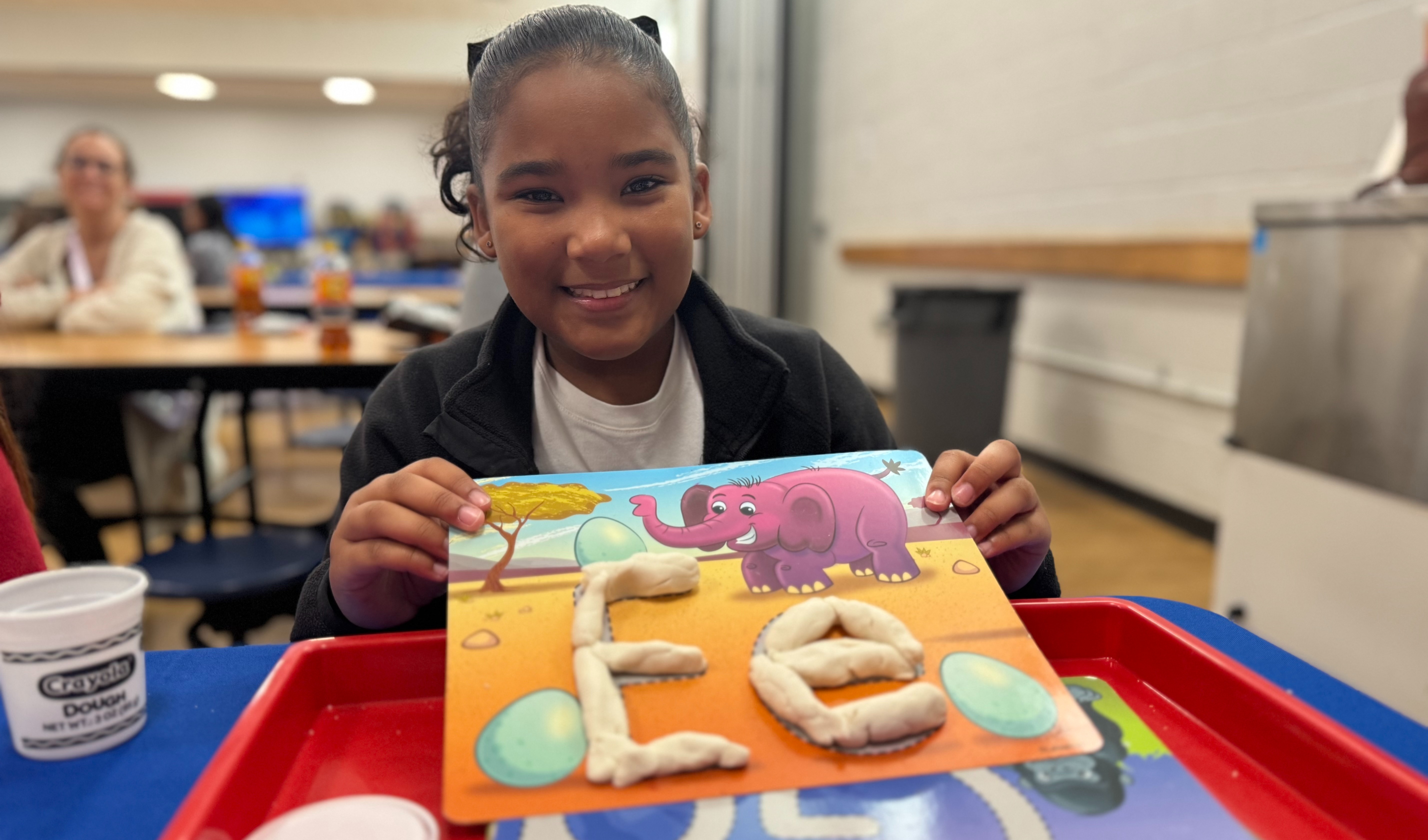 A student is smiling while showing a letter activity made with modeling dough at a school family engagement event.