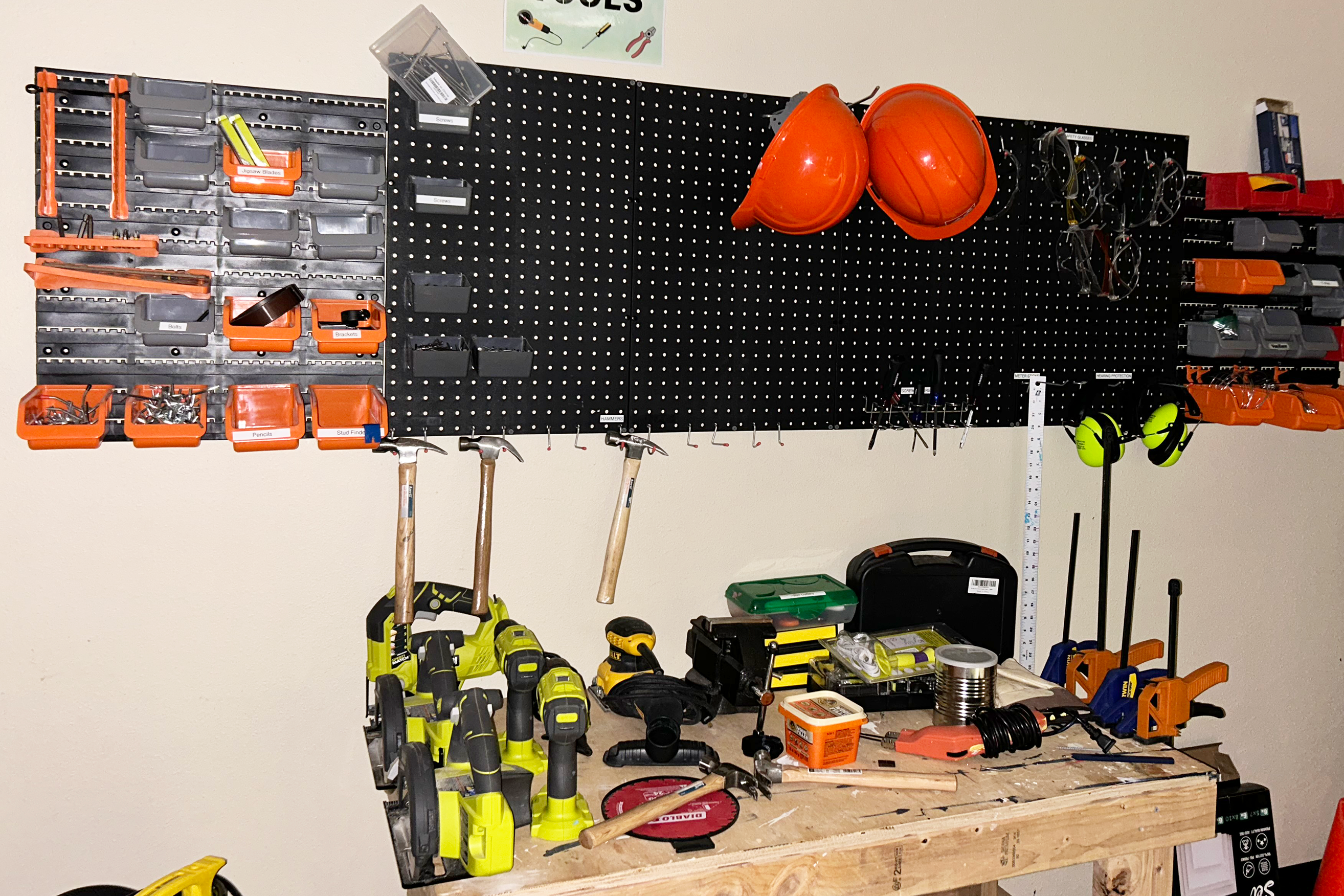Power tools and hand tools hanging on a wall and on a wooden table.