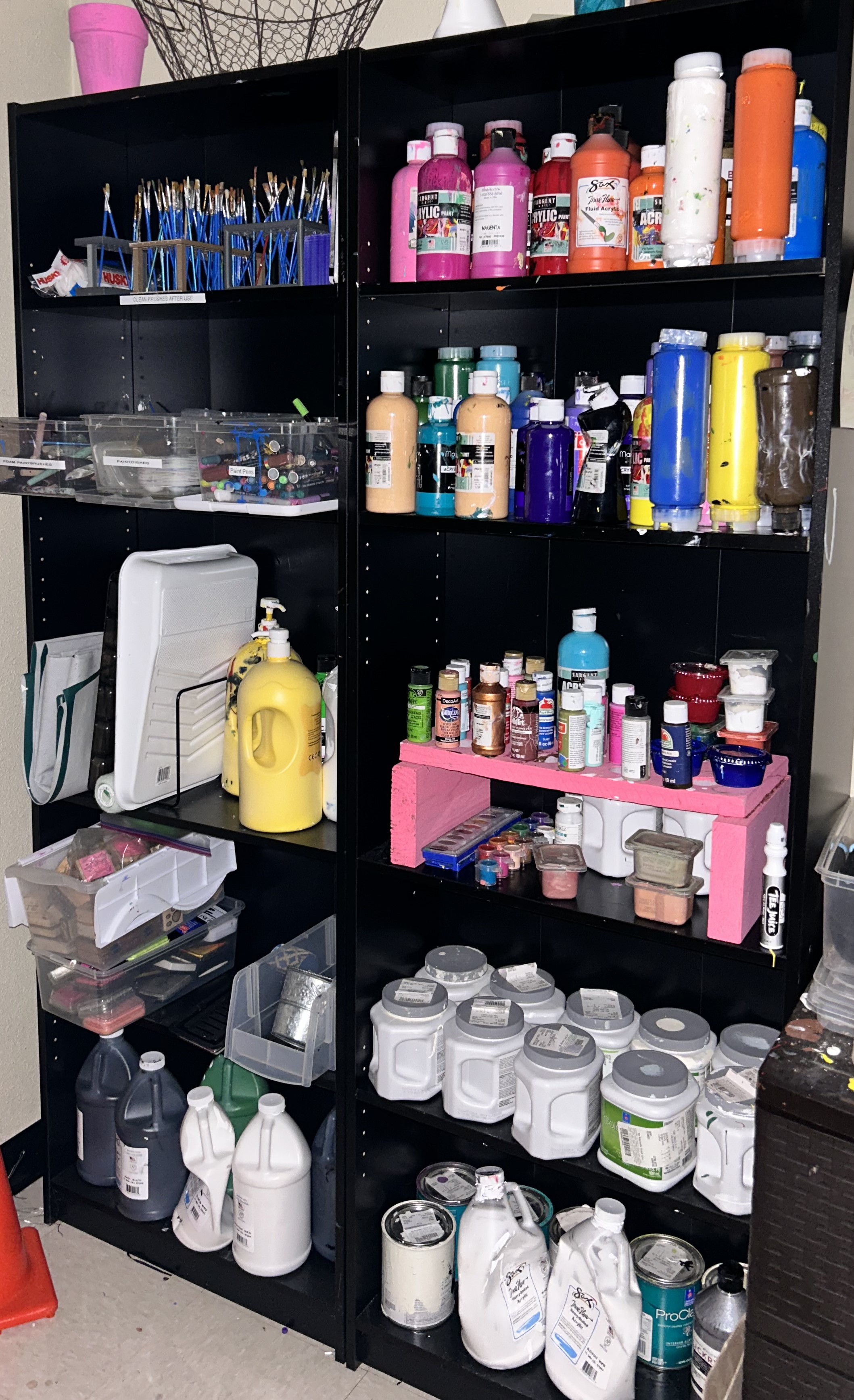 Various paint supplies on two black bookshelves.