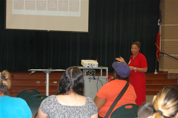 person presenting information in a classroom setting, surrounded by an audience.