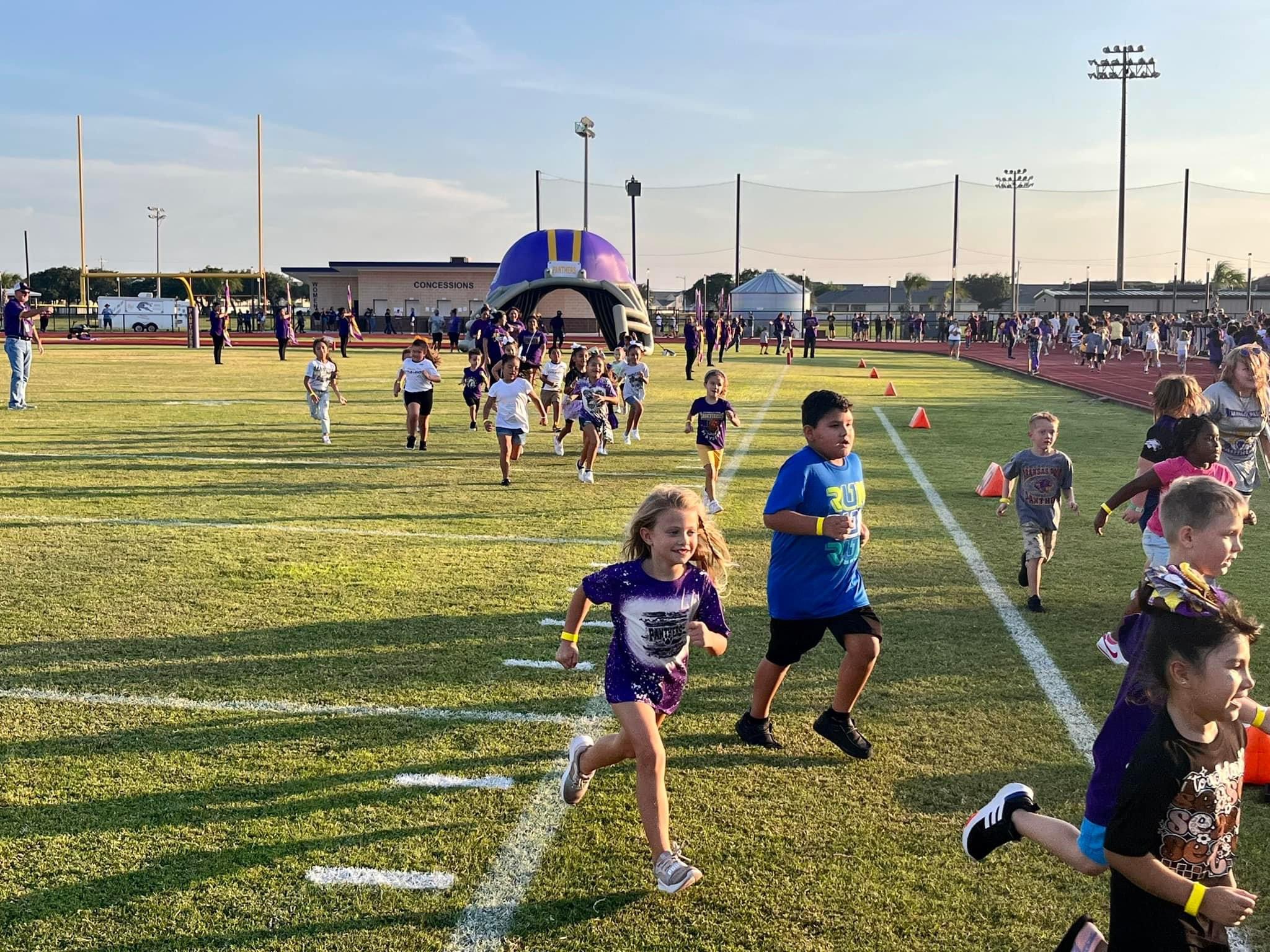 large group of students running out of a football helmet run-through tunnel across a football field