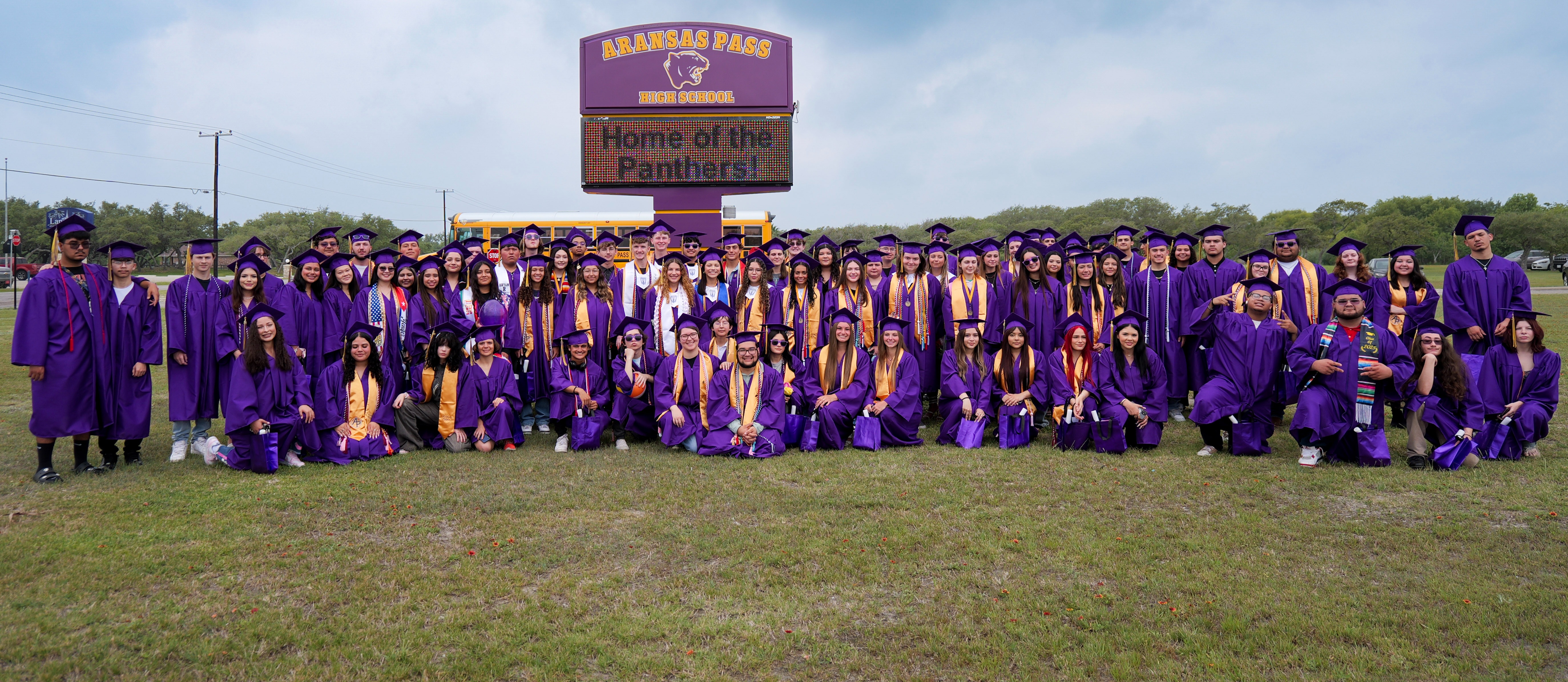 group of students in graduation caps and gowns in front of a digital marquee outdoors