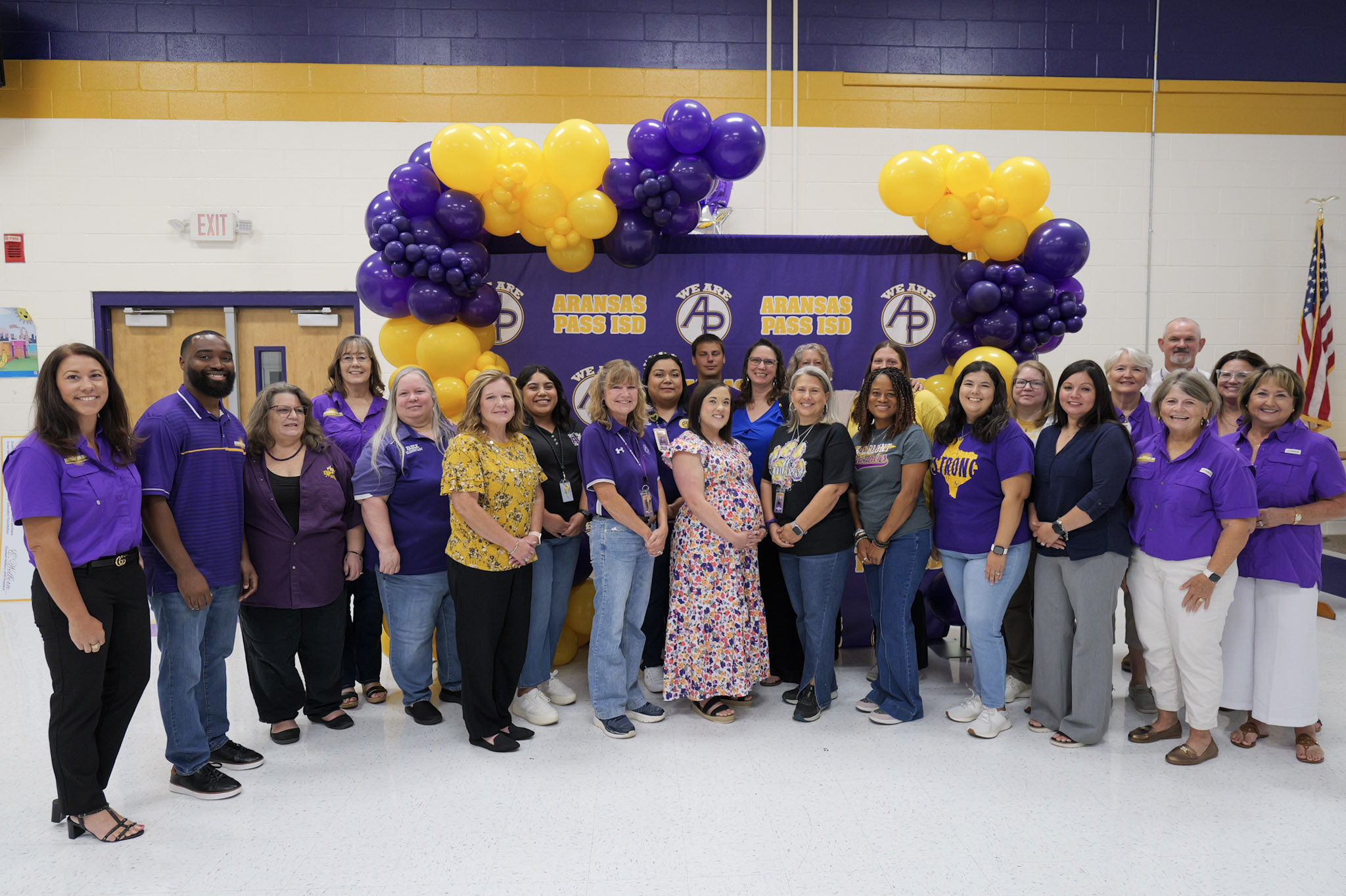 group of people standing in front of a purple and gold backdrop with balloons