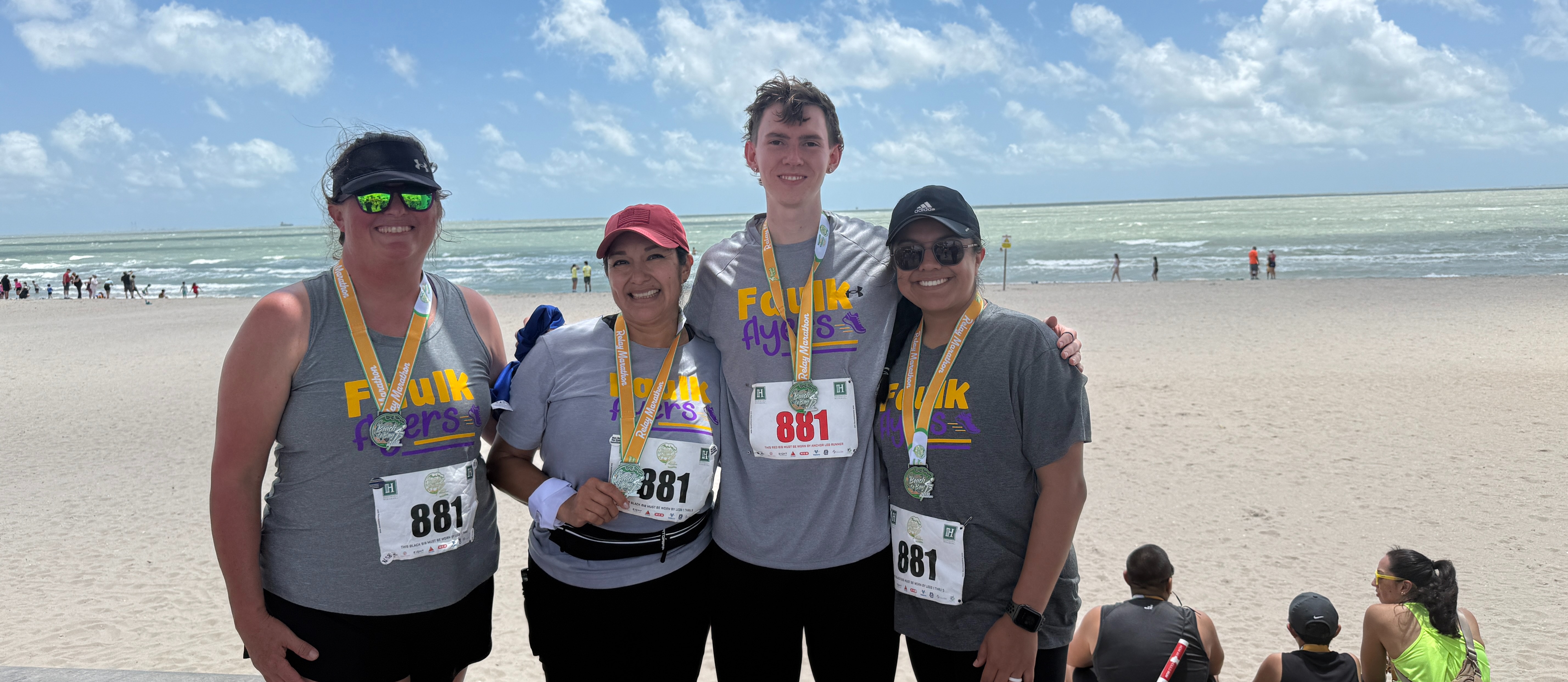 four teachers in front of a beach wearing marathon bibs for the Beach to Bay relay