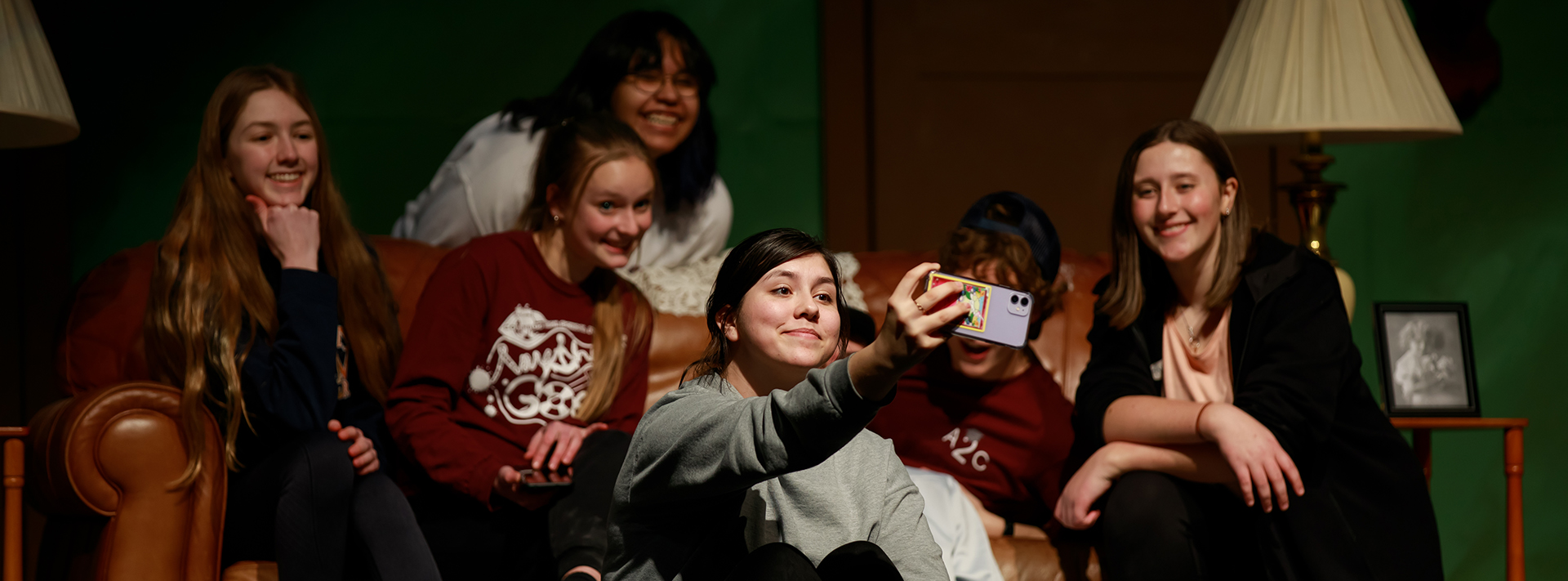 A CHS student sits on stage and frames a selfie with friends.