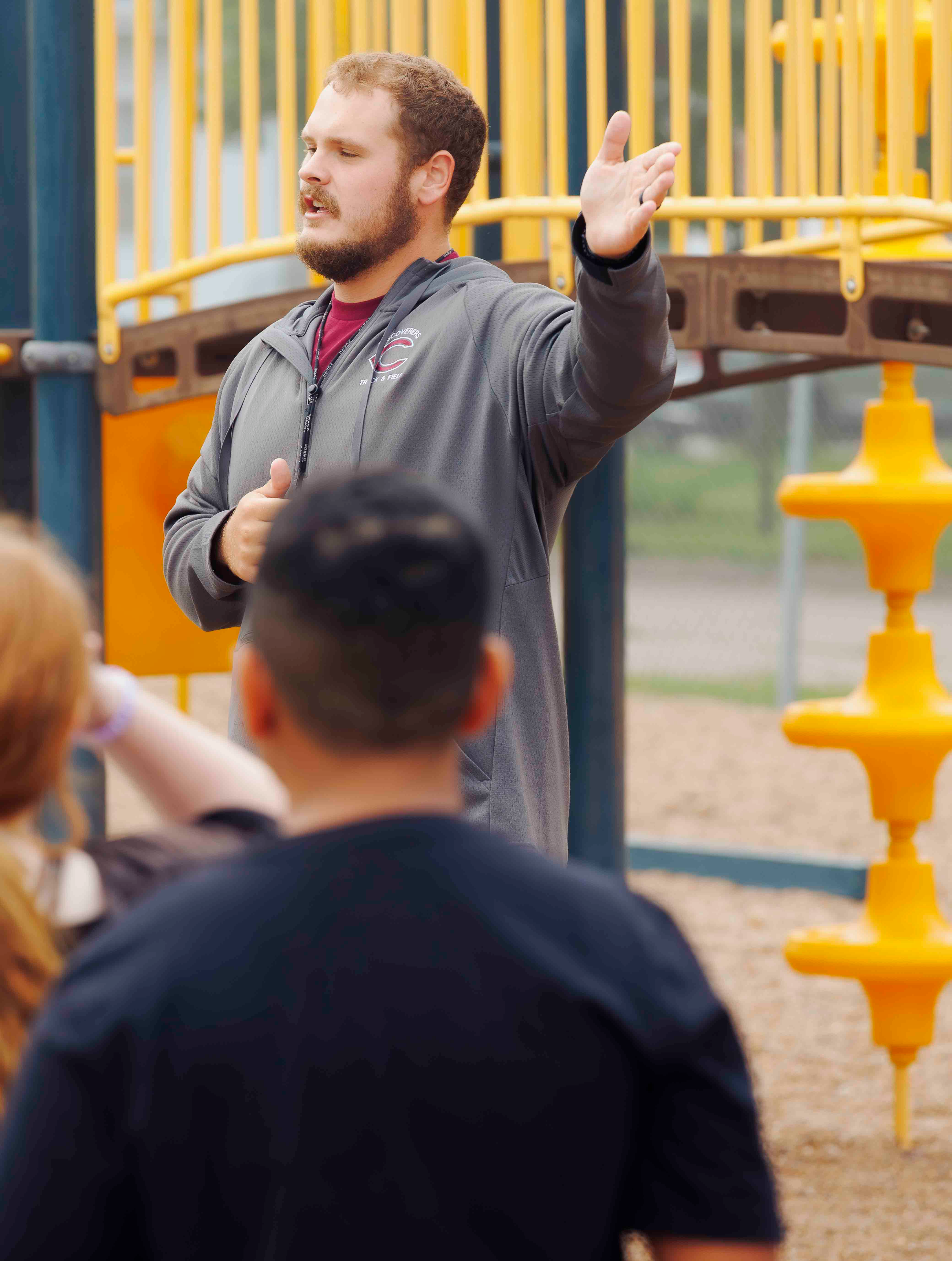 An elementary teacher points off camera in front of the playground equipment at Emerson Elementary School.