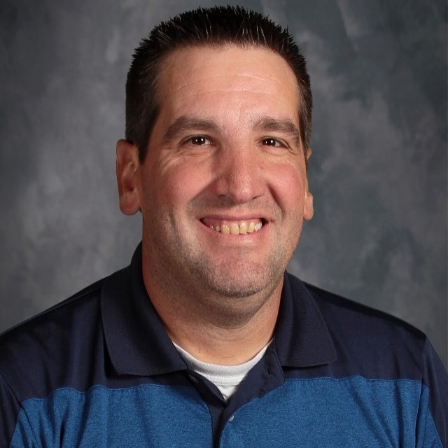 Jimmy Johnson, a man with two-tone blue shirt,  short black hair and stubble smiles in a posed pictured. 