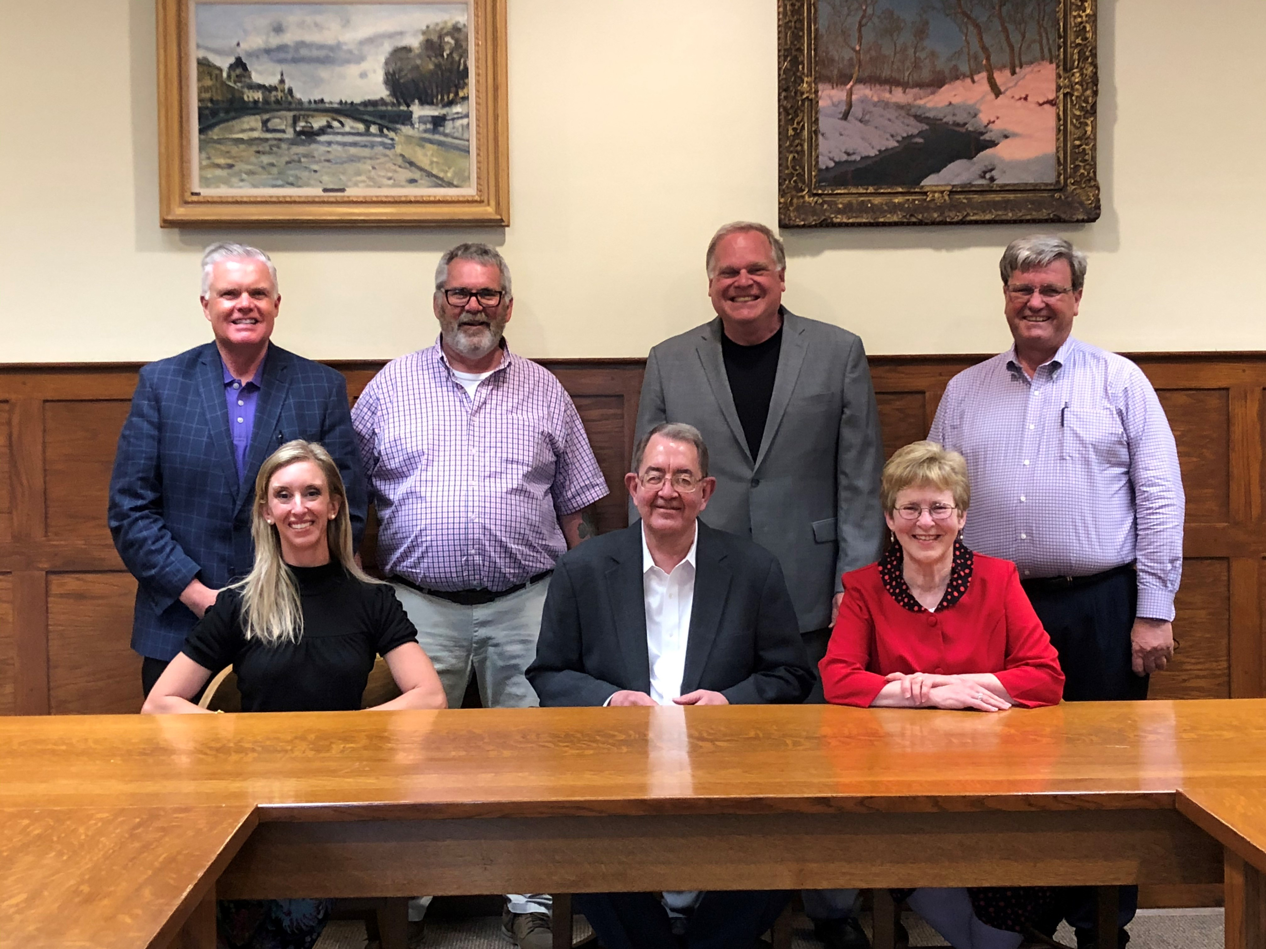 Four Board Members standing in the back and 3 Board Members sitting in the front facing the front smiling