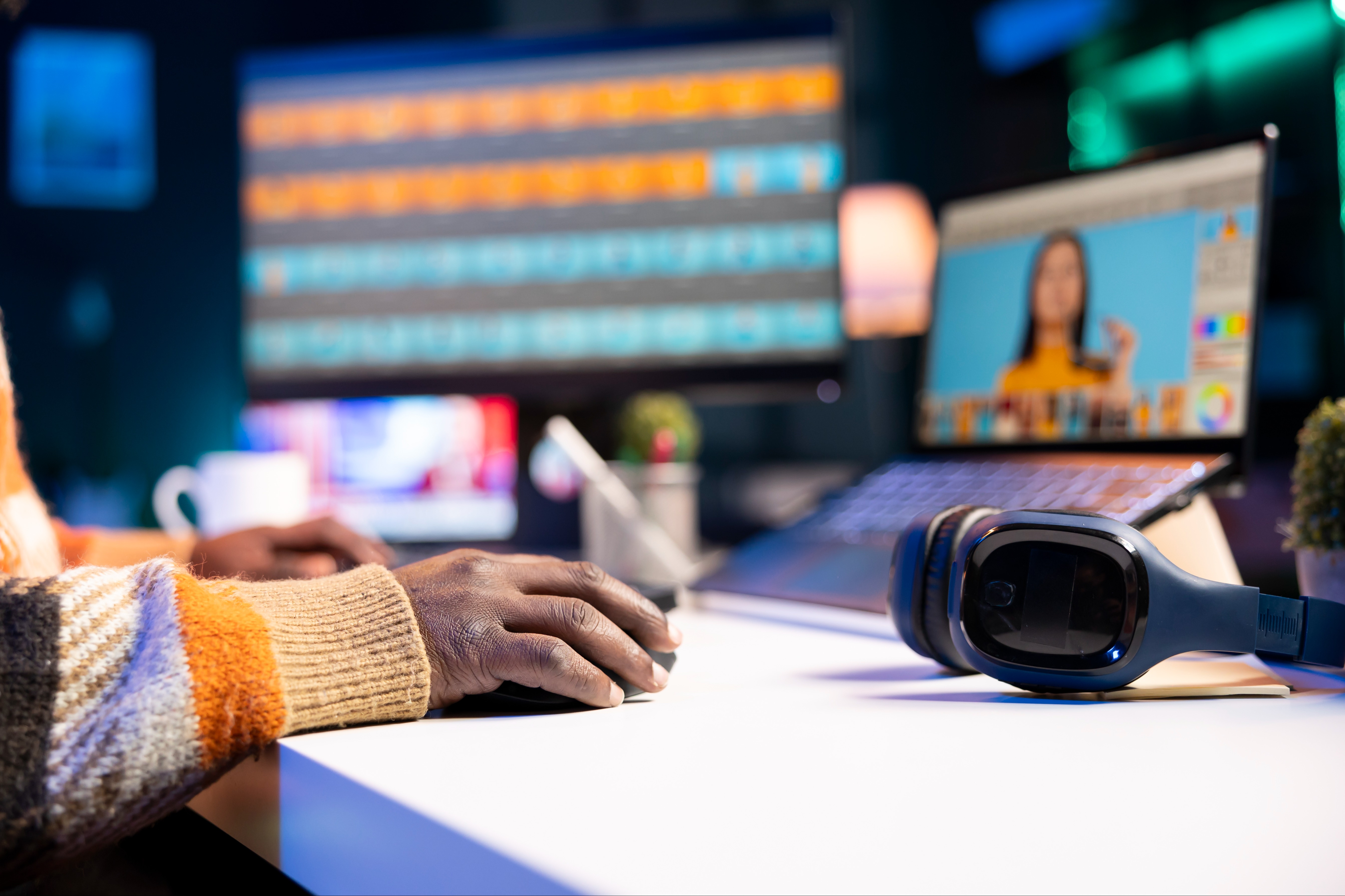 hand on computer mouse looking at computer screens with headphones in foreground
