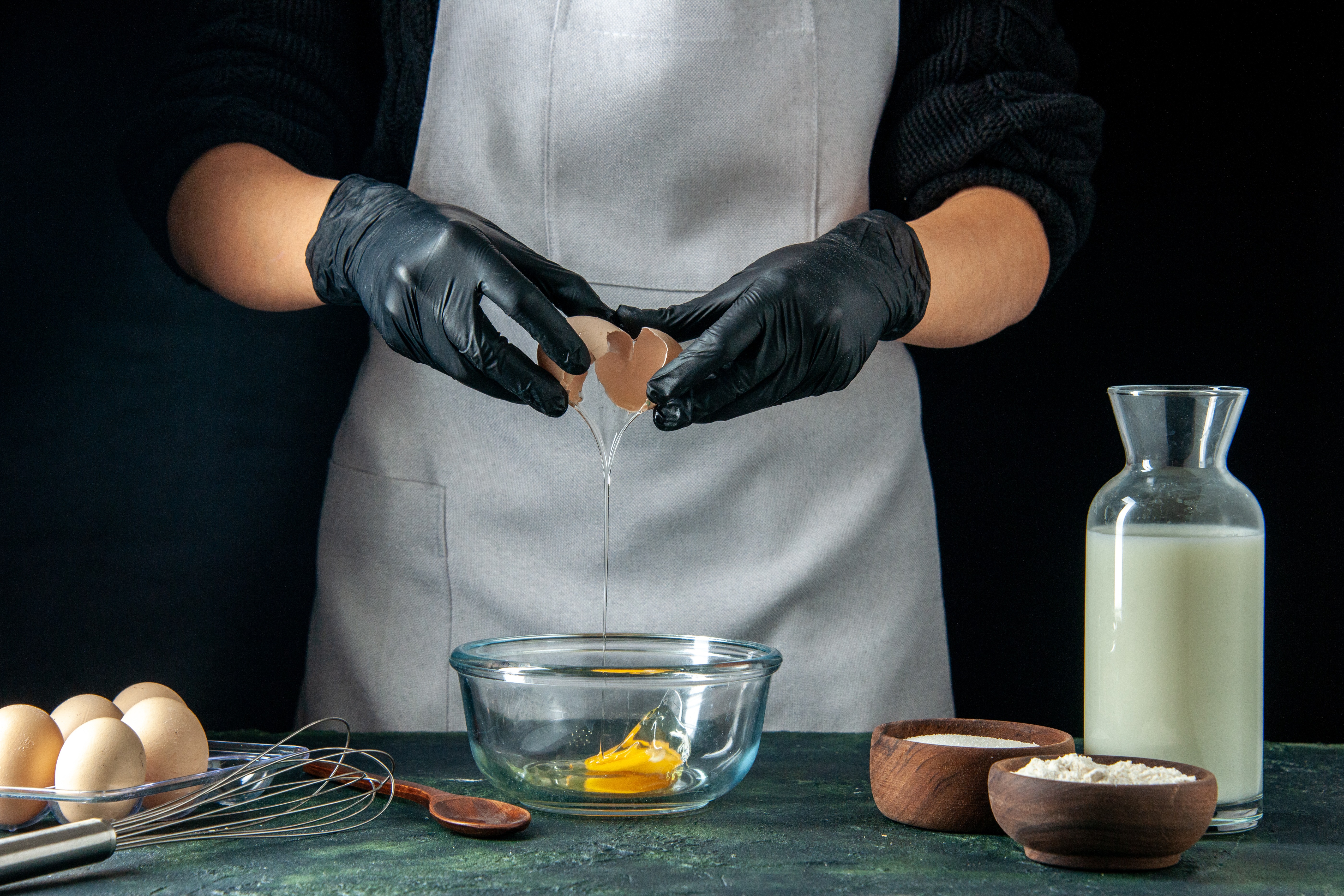 chef cracking an egg over a bowl with other ingredient on table