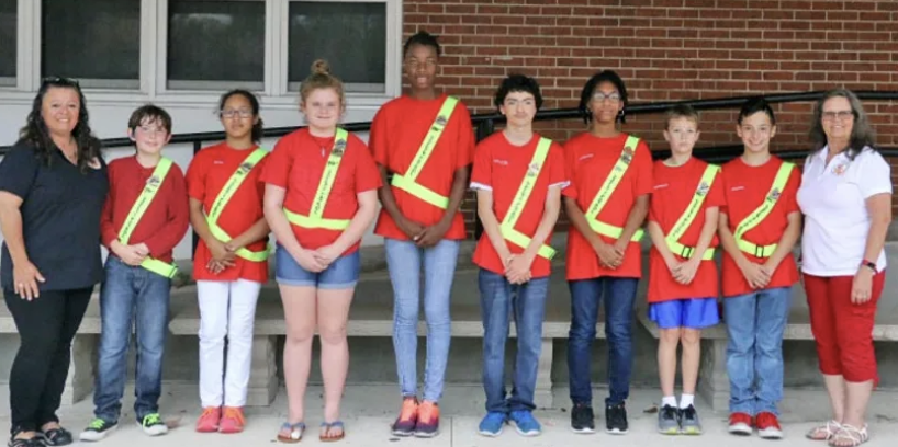 group of students each wearing uniforms smiling to the camera next to teachers