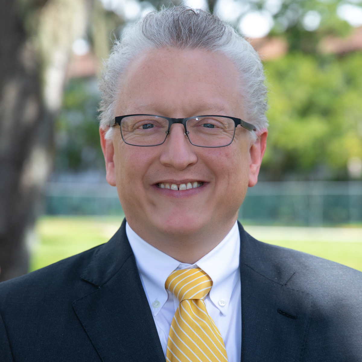 Matt Kramer wearing glasses, white shirt, yellow striped tie and dark gray blazer.