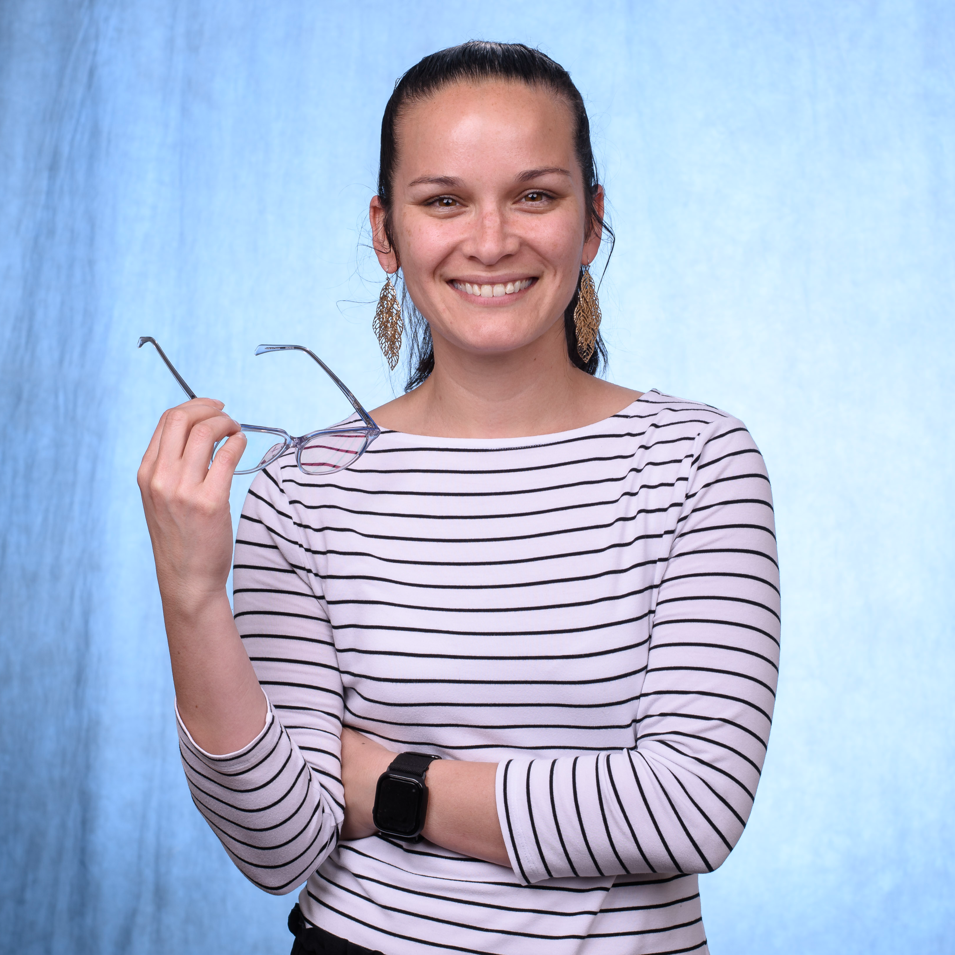 Jay Girton wearing a white shirt with black stripes, holding glasses in her hand.