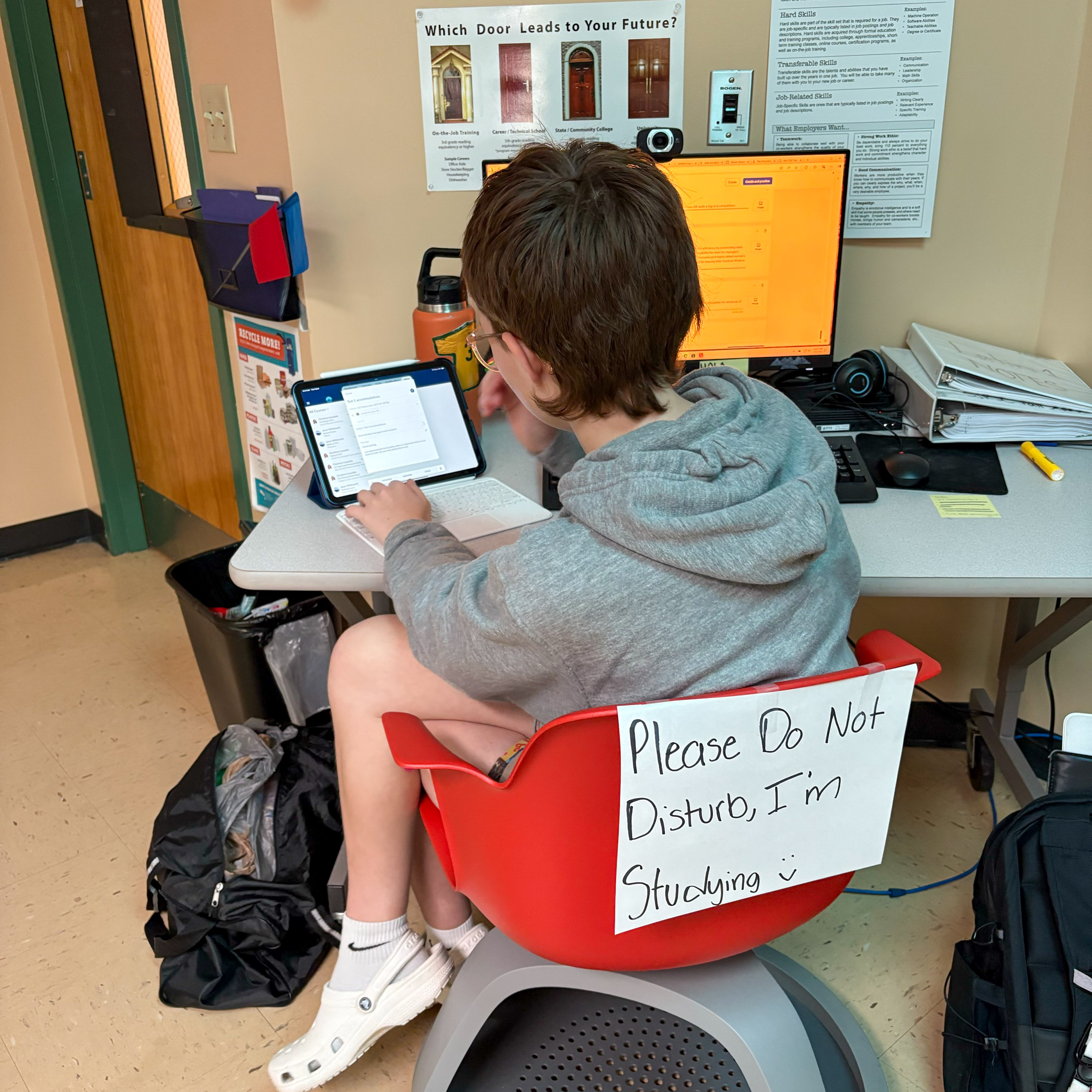 A student working on a laptop with a sign on the back of her seat that reads, "Please Do Not Disturb, I'm Studying."