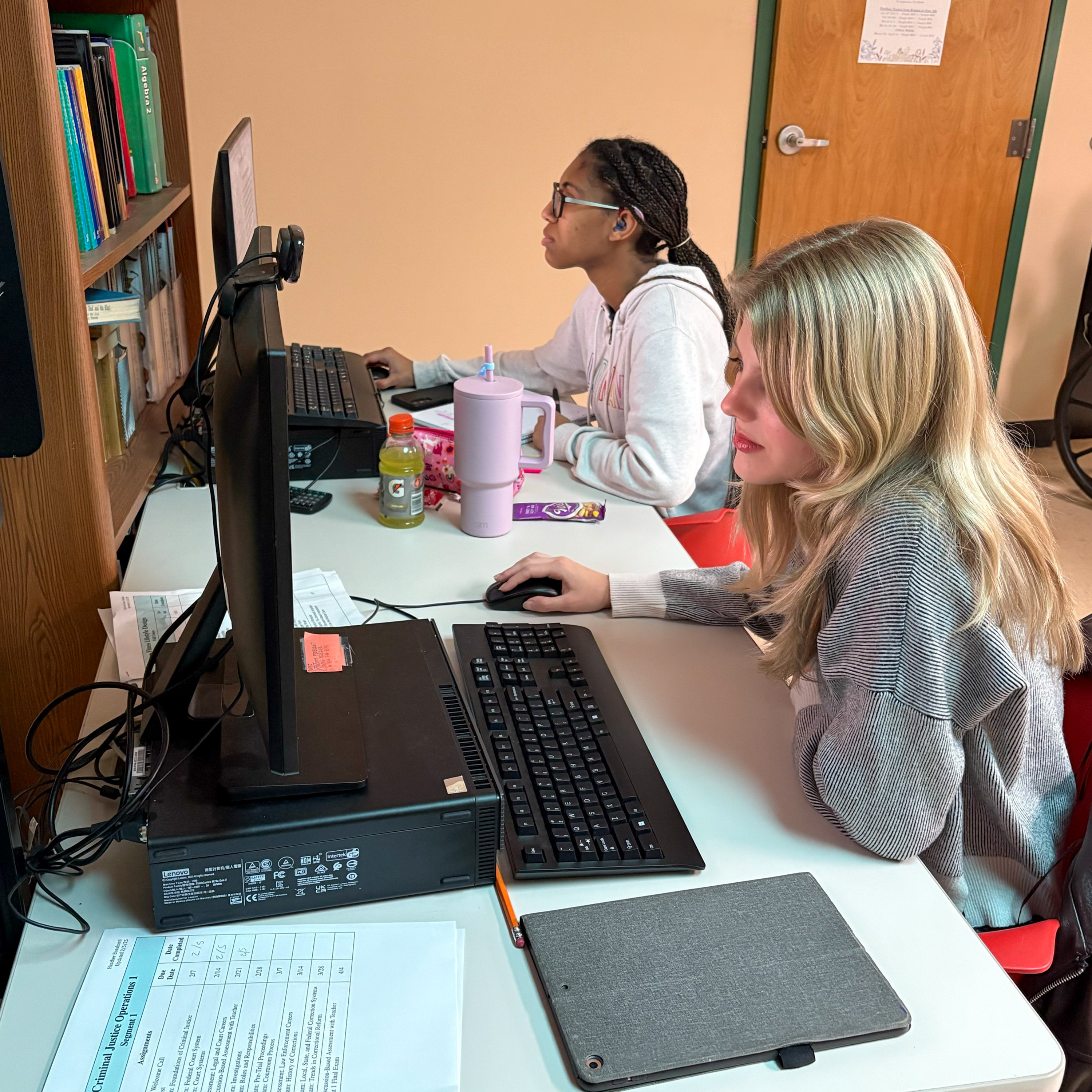 Two deaf girls sitting at computers, completing an online course.