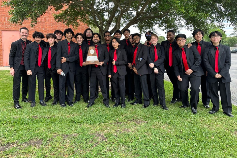 A group of students in matching black suits and red ties poses for a photo under a tree.