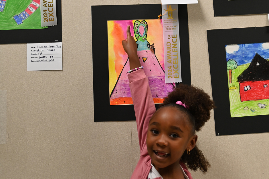 A young girl with pink clothing points at a colorful painting. A sign with "2024 Award Excellence" hangs above.
