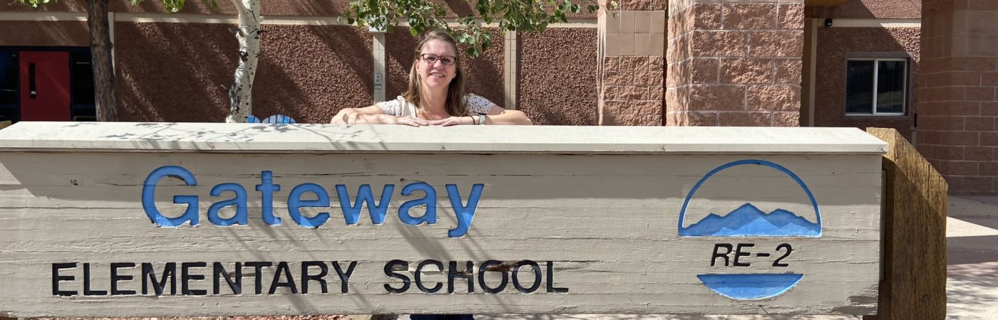 principal standing outside of school behind the school sign