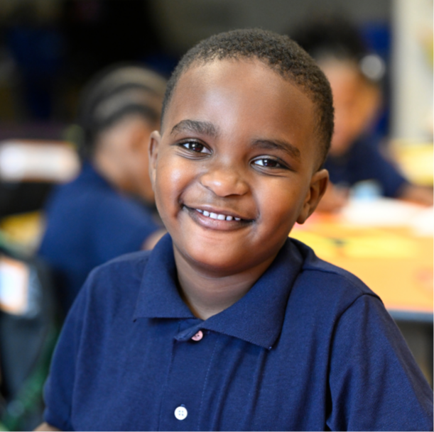 a child smiles at the camera while sitting at a table